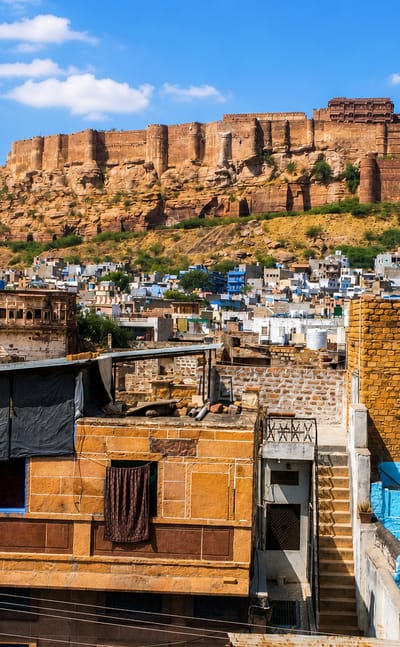 Mehrangarh Fort towers on its rocky hill above Jodhpur's blue-painted houses under a blue sky.