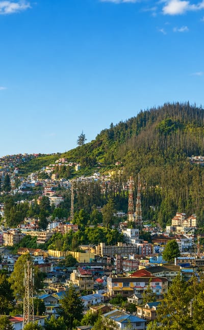 Colourful hillside houses of Ooty spread across forested Nilgiri slopes under a blue sky