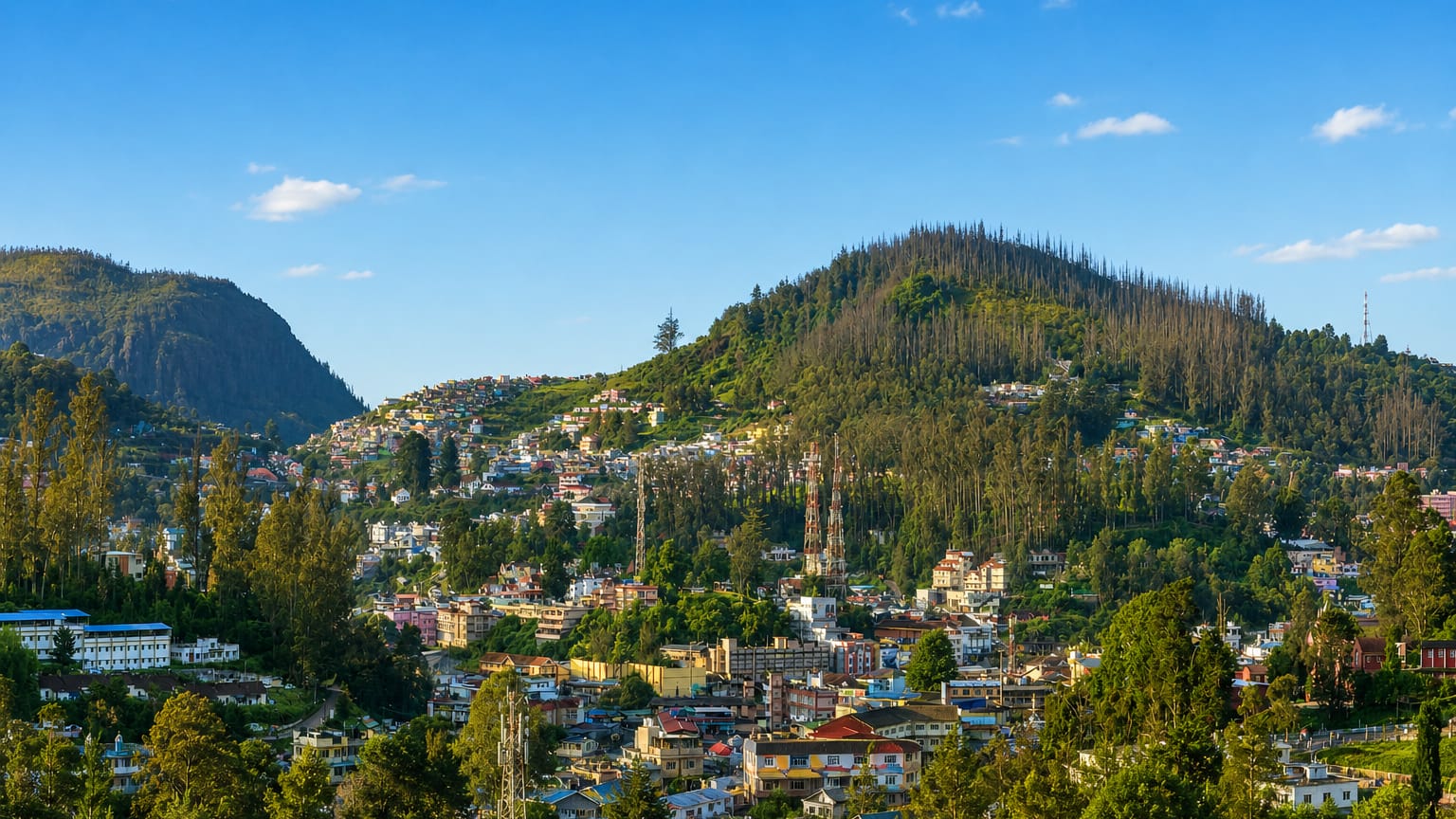 Colourful hillside houses of Ooty spread across forested Nilgiri slopes under a blue sky
