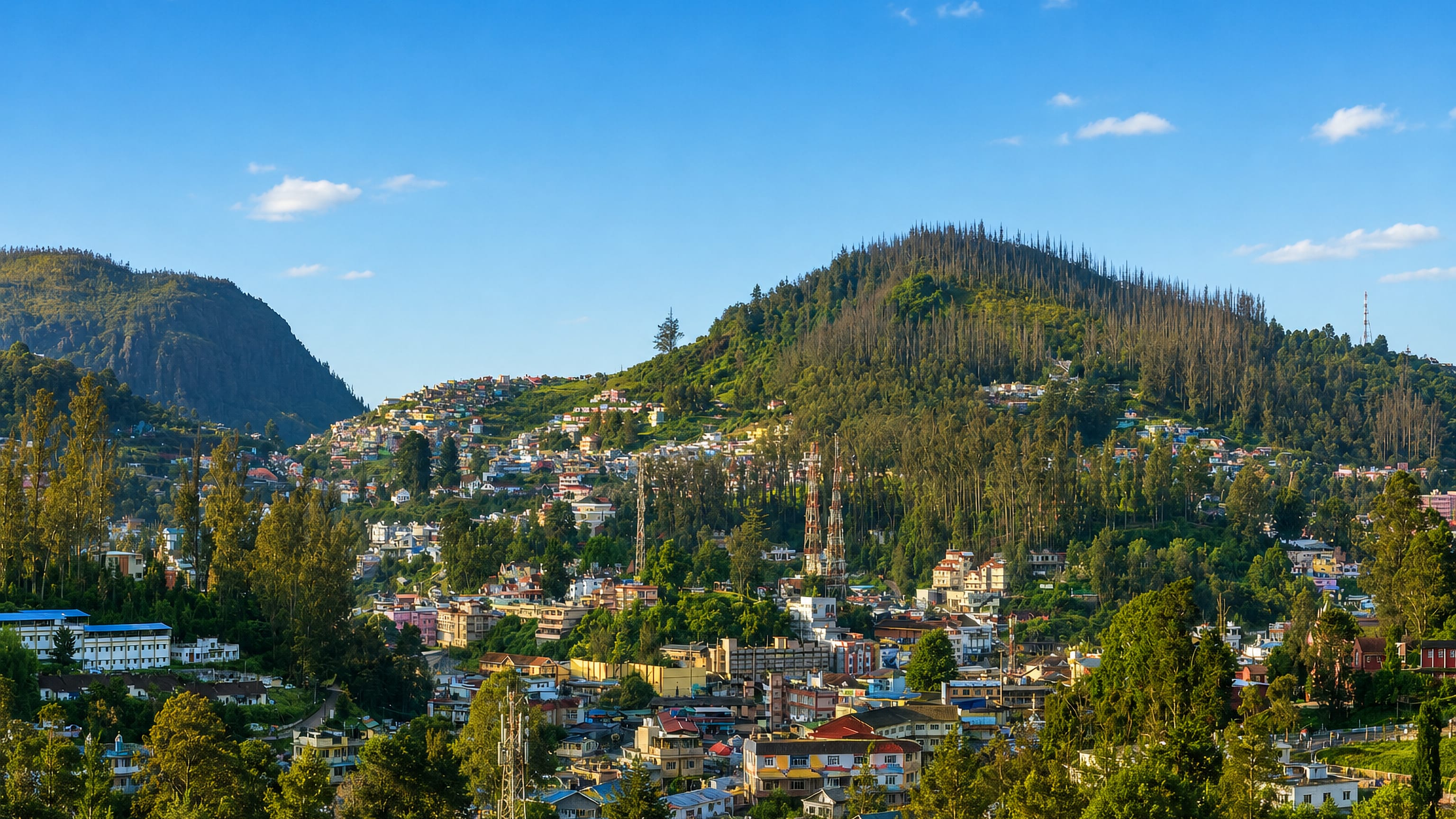 Colourful hillside houses of Ooty spread across forested Nilgiri slopes under a blue sky