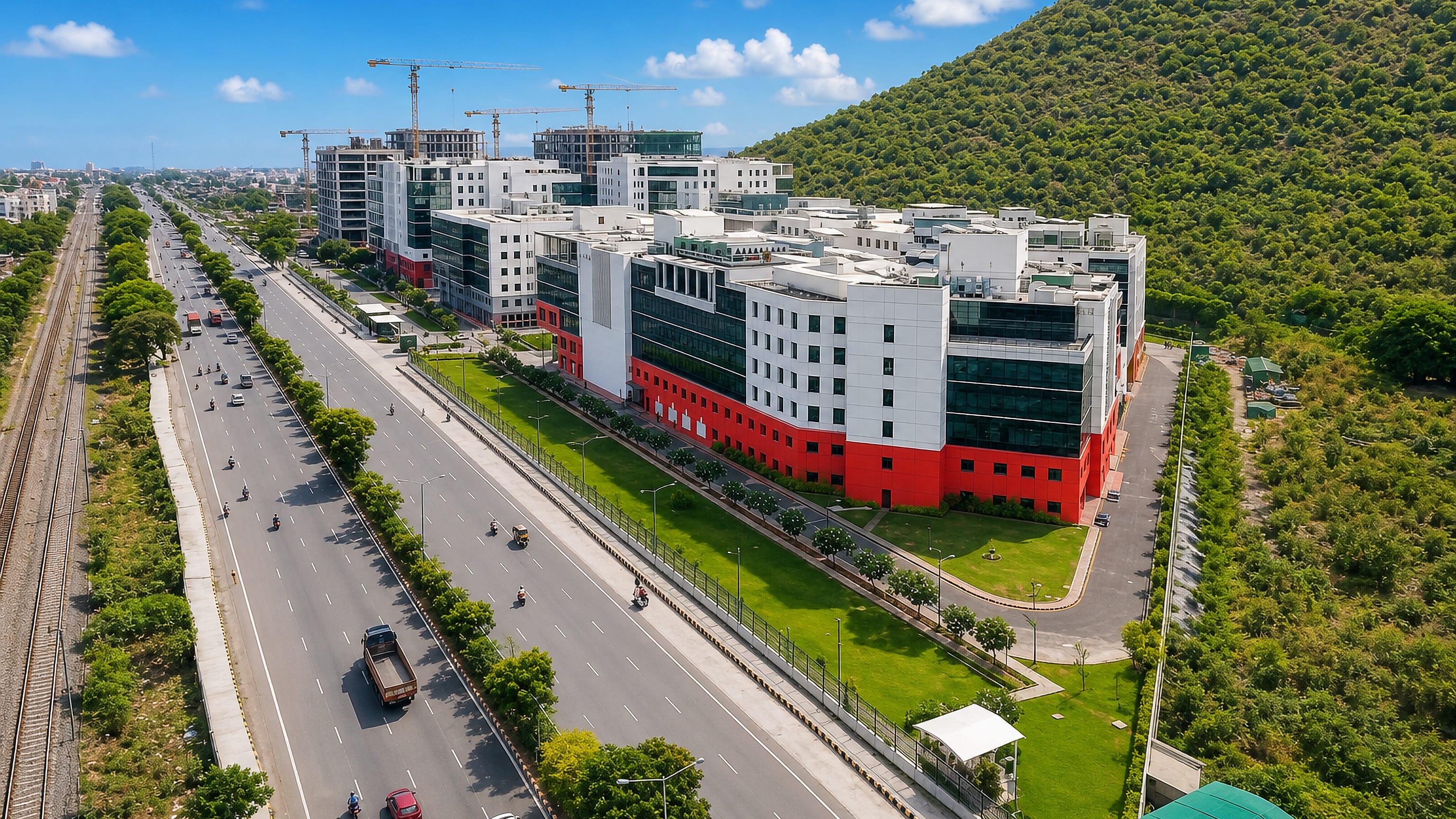 Aerial of a divided highway and railway beside a red-and-white office campus at Tambaram, Chennai, India
