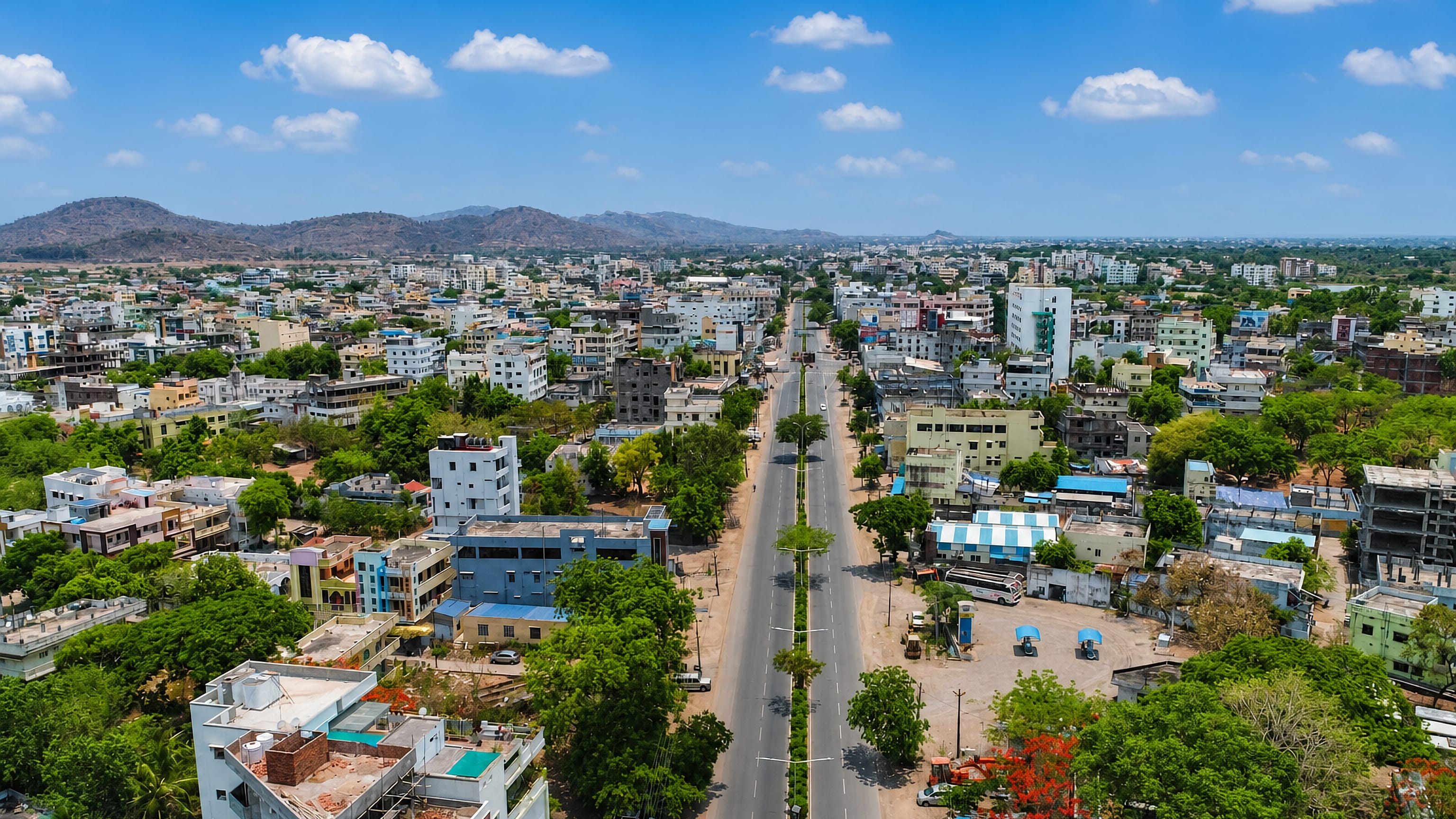 Aerial view of Mancherial, Telangana, with a tree-lined divided highway running through the town toward distant hills.