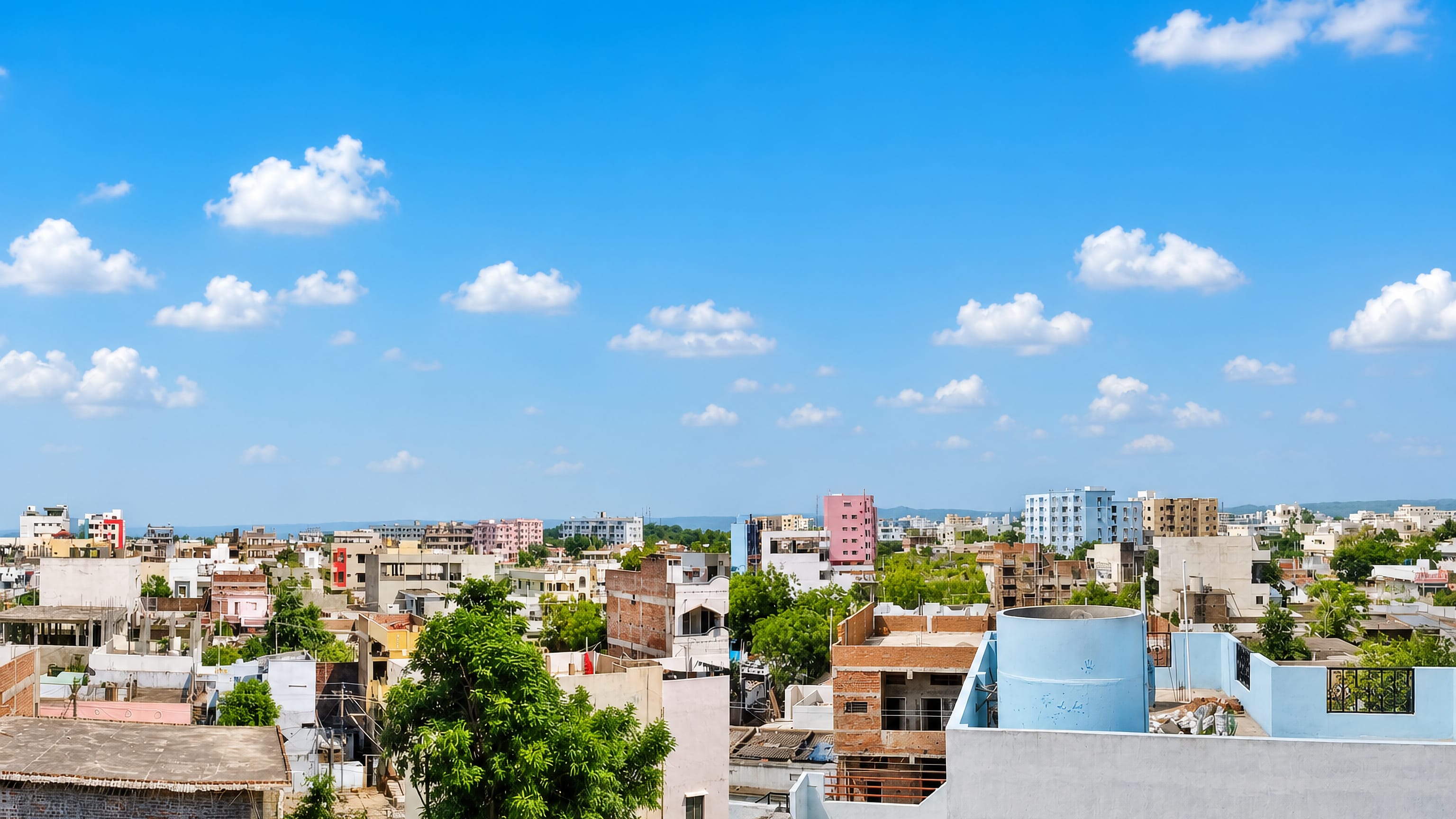 Rooftop view across Nizamabad, Telangana, with concrete and brick houses, water tanks and low hills on the horizon.