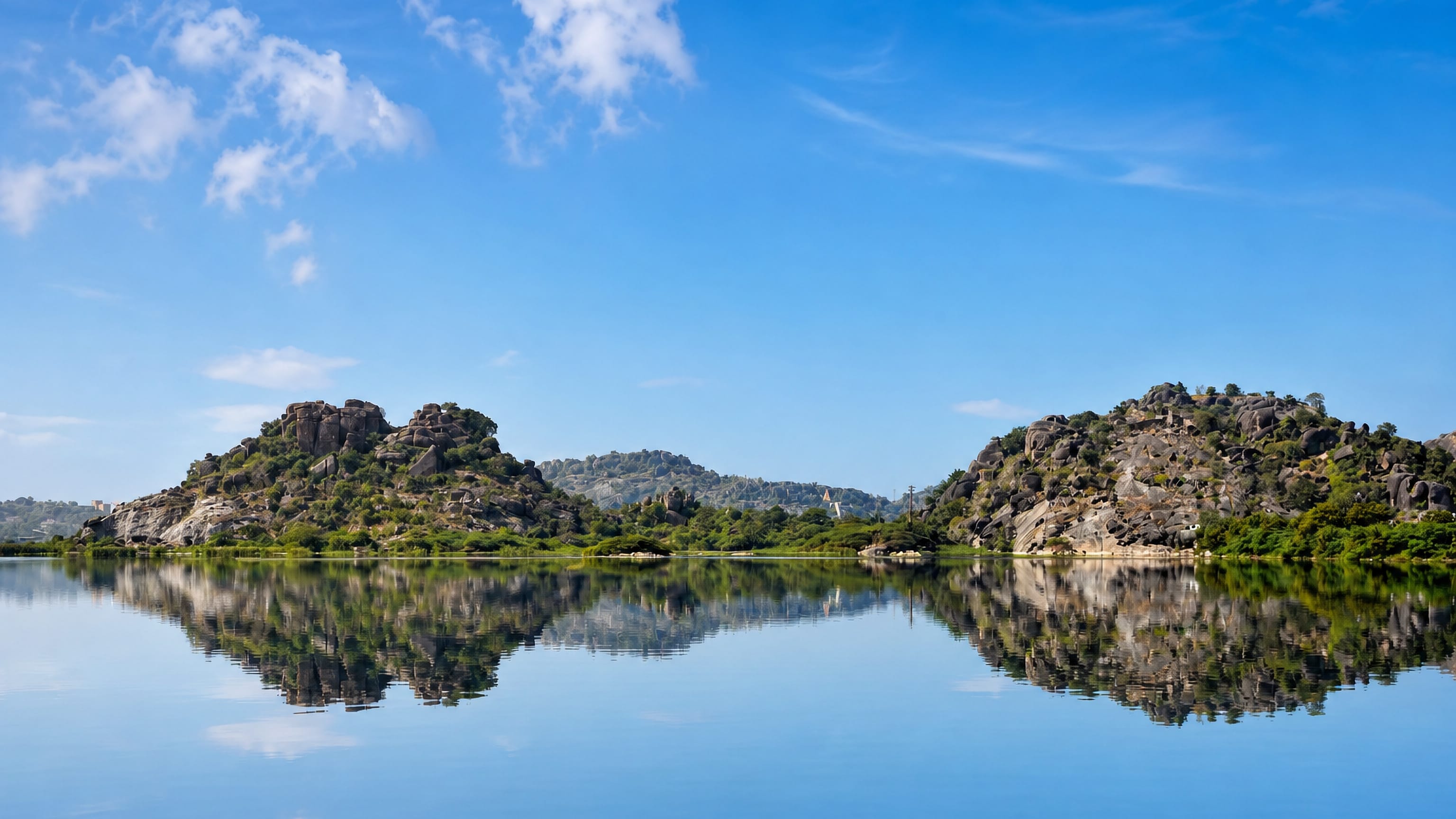 Granite boulder hills and greenery mirrored in a still lake on the edge of Warangal, Telangana.