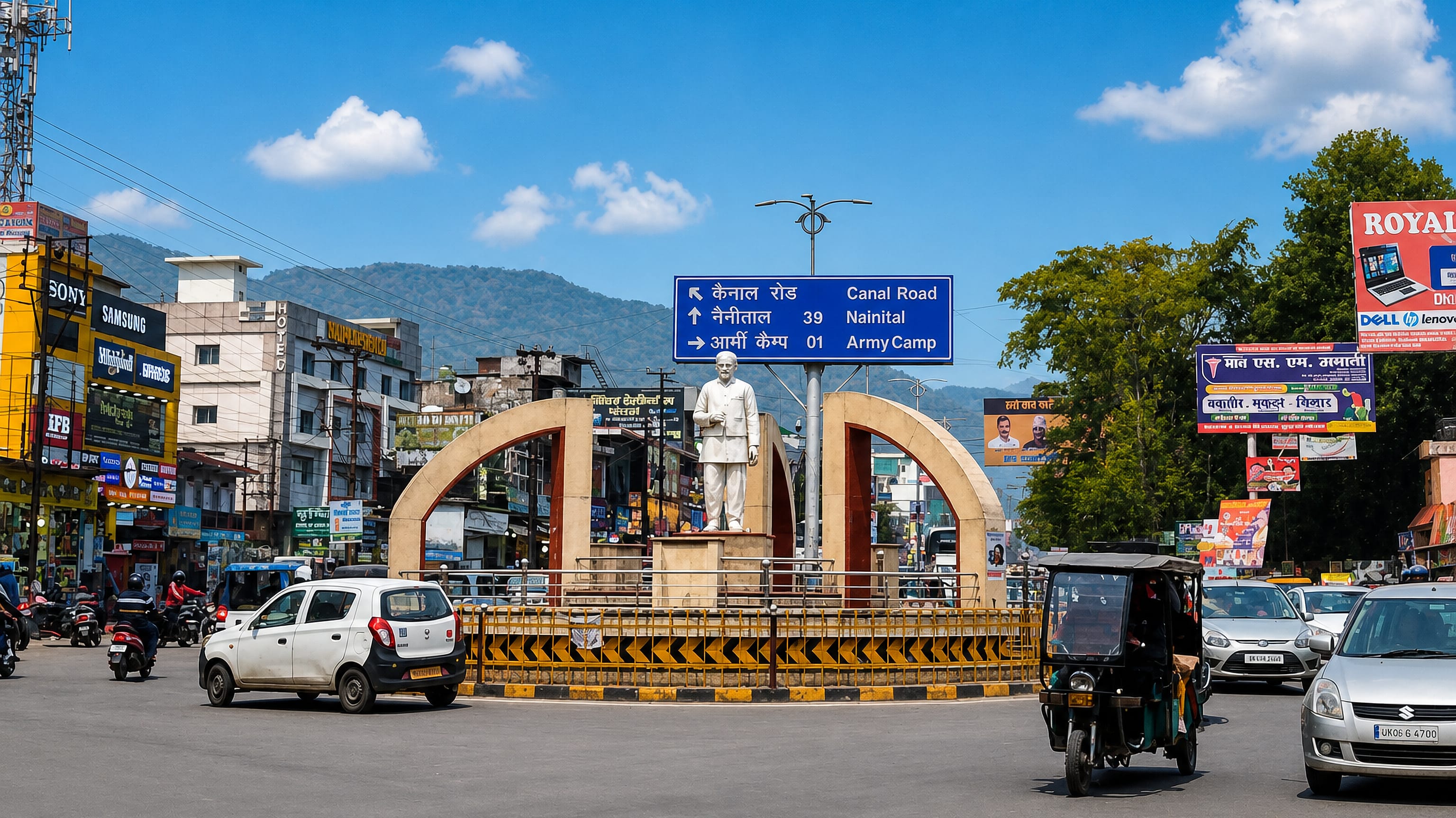 Traffic circles a statue and twin arches at a shop-lined Haldwani junction below the Kumaon foothills.