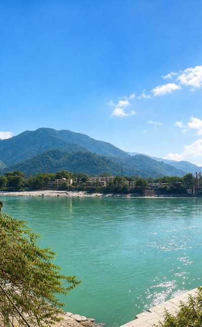 The turquoise Ganges at Rishikesh with a suspension bridge and forested hills