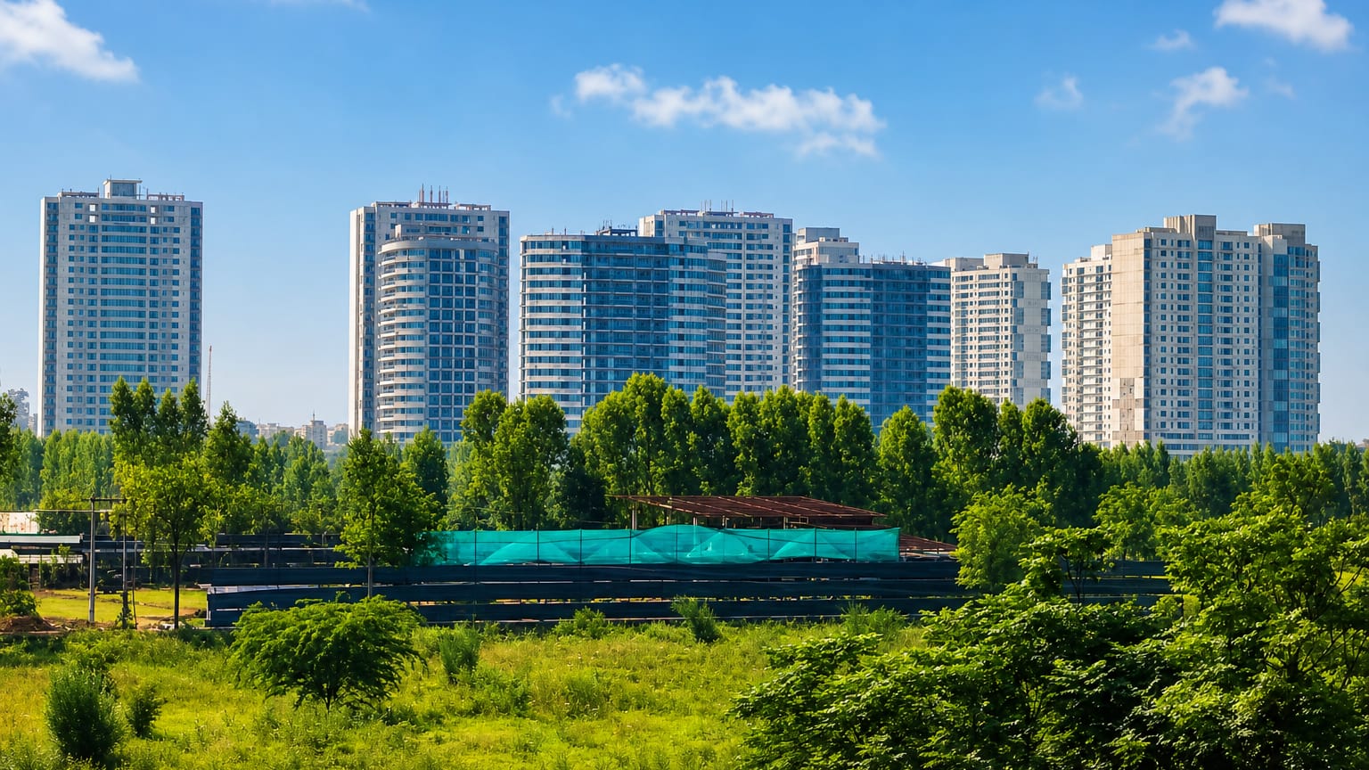 Modern residential high-rise towers behind green trees and open parkland in Chandigarh, India.