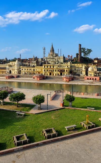 Ayodhya's Ram ki Paidi ghats and temple-crowned skyline along the Sarayu river under a blue daytime sky.