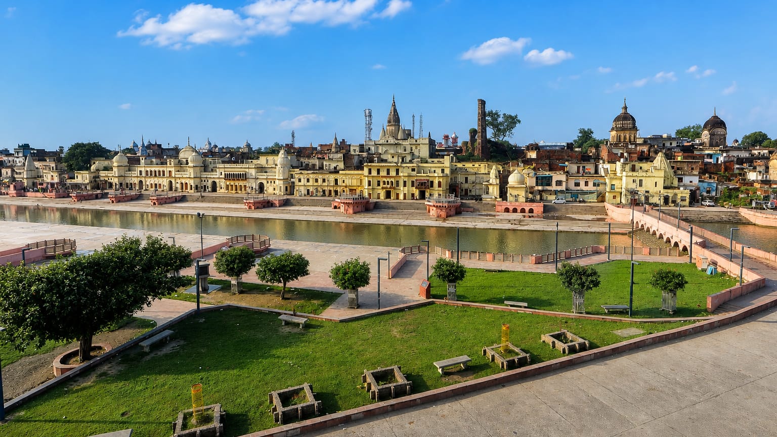 Ayodhya's Ram ki Paidi ghats and temple-crowned skyline along the Sarayu river under a blue daytime sky.