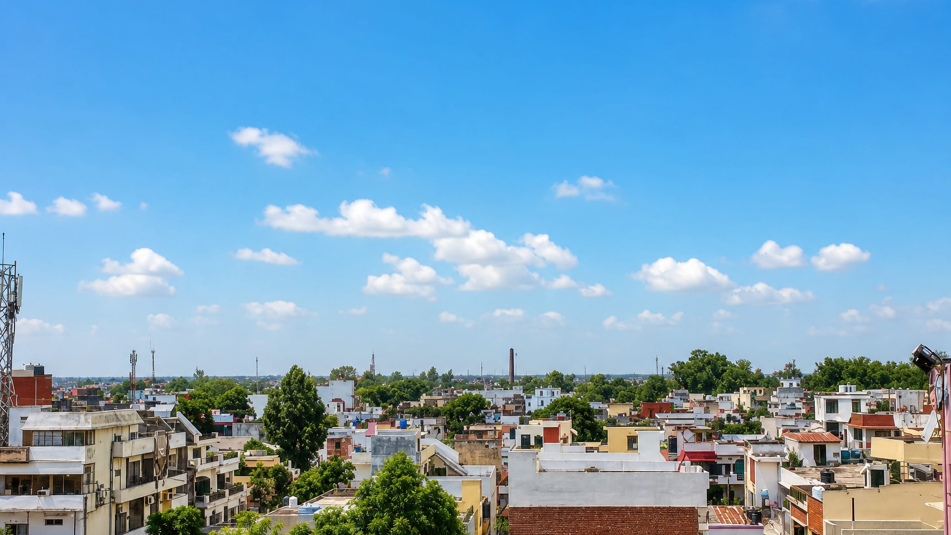 Rooftop view across Bareilly's low-rise houses, water tanks and leafy streets under a summer sky.