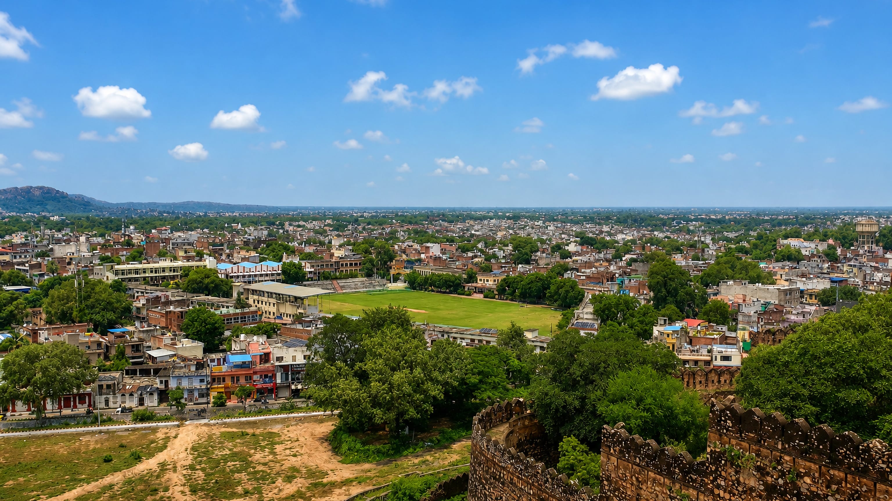 Jhansi, Uttar Pradesh, viewed from the fort ramparts across rooftops and a green maidan to distant hills.