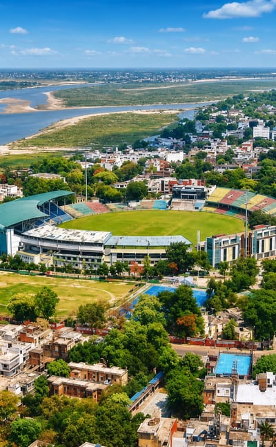 Aerial view of a cricket stadium beside the Ganges River amid Kanpur's greenery and city streets.