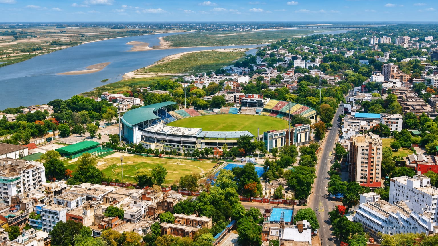 Aerial view of a cricket stadium beside the Ganges River amid Kanpur's greenery and city streets.