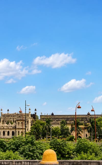Lucknow's Bara Imambara complex with tall minarets and domes rising above lush greenery under a blue sky