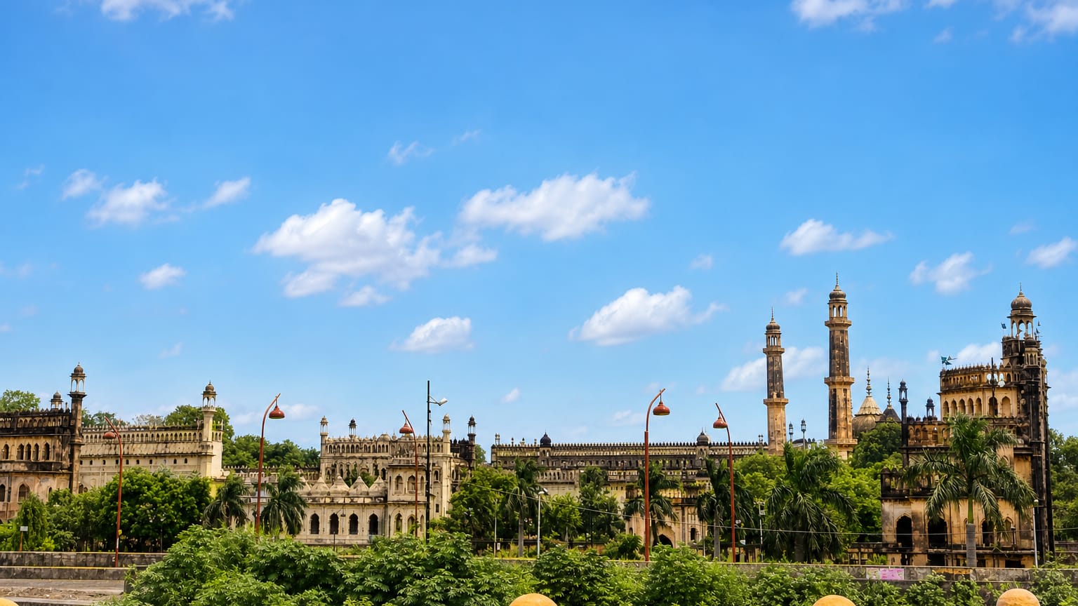 Lucknow's Bara Imambara complex with tall minarets and domes rising above lush greenery under a blue sky