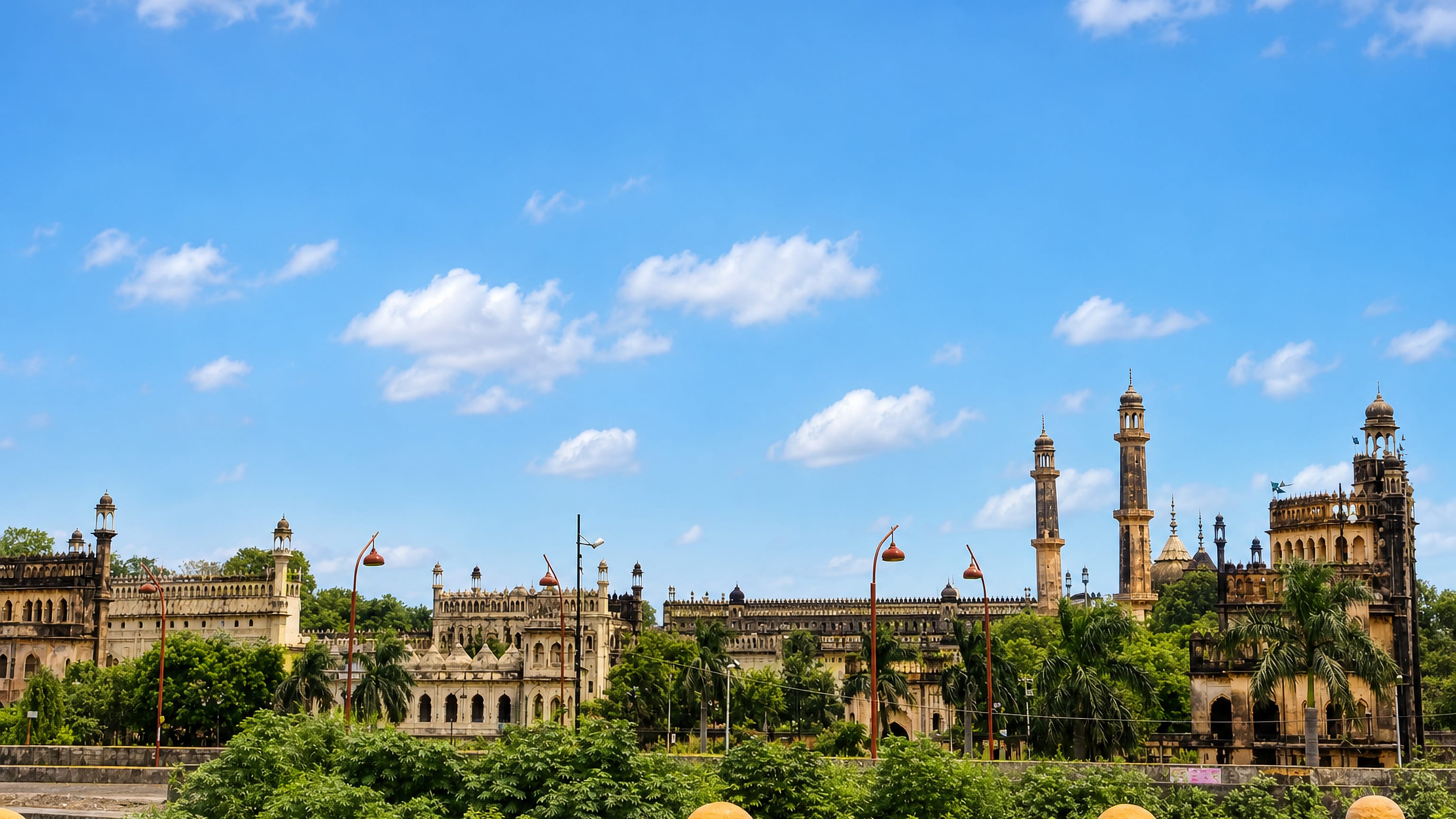 Lucknow's Bara Imambara complex with tall minarets and domes rising above lush greenery under a blue sky