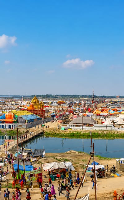 Vast riverside festival grounds at Prayagraj with colourful temples and tents lining the Ganges-Yamuna confluence