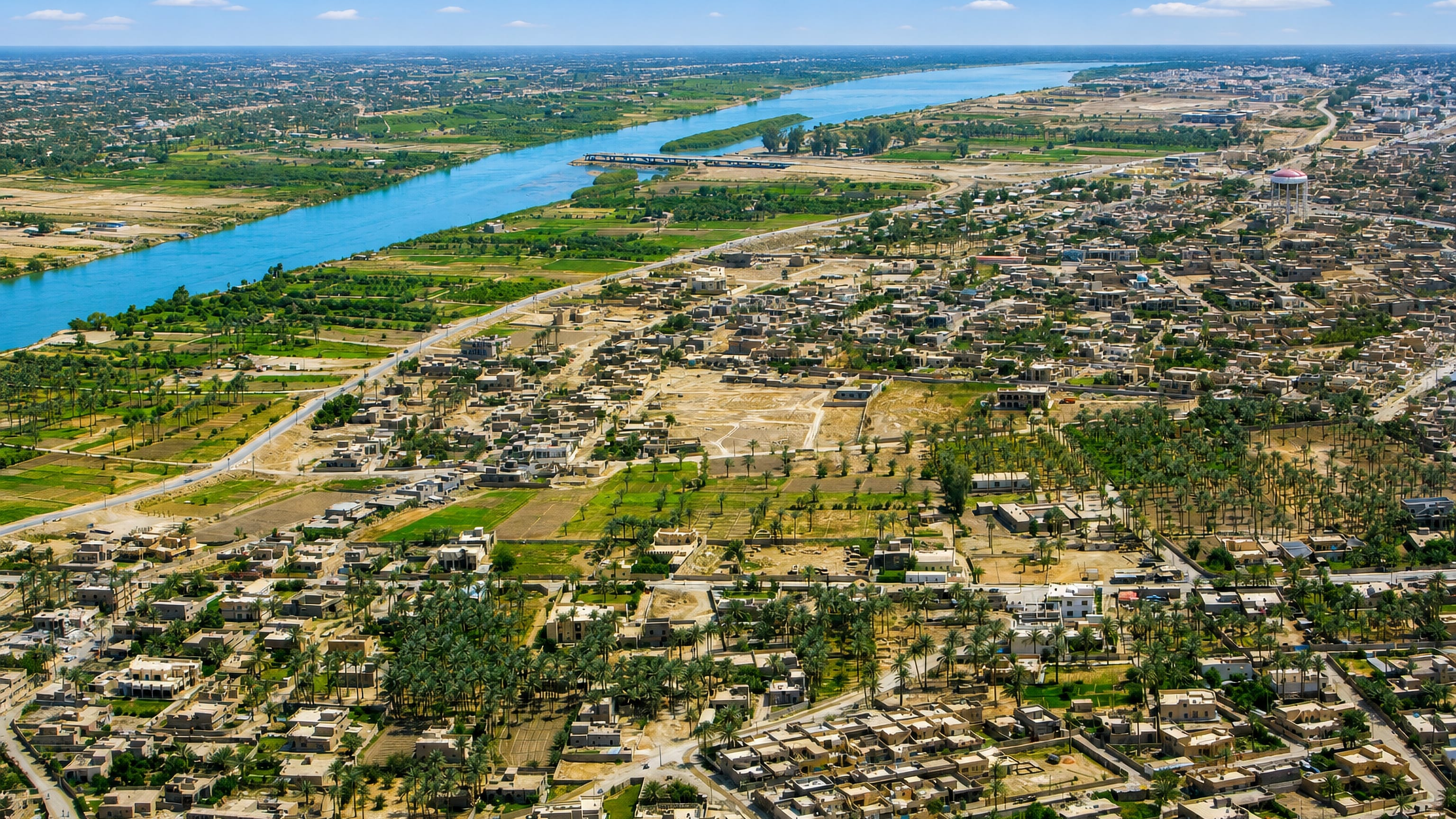 Aerial view of Ramadi's low-rise houses and palm groves along the wide blue Euphrates in Iraq.