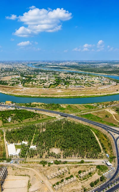 Aerial view of the Tigris river bend and highway interchanges past Dora district in Baghdad, with a power station on the horizon