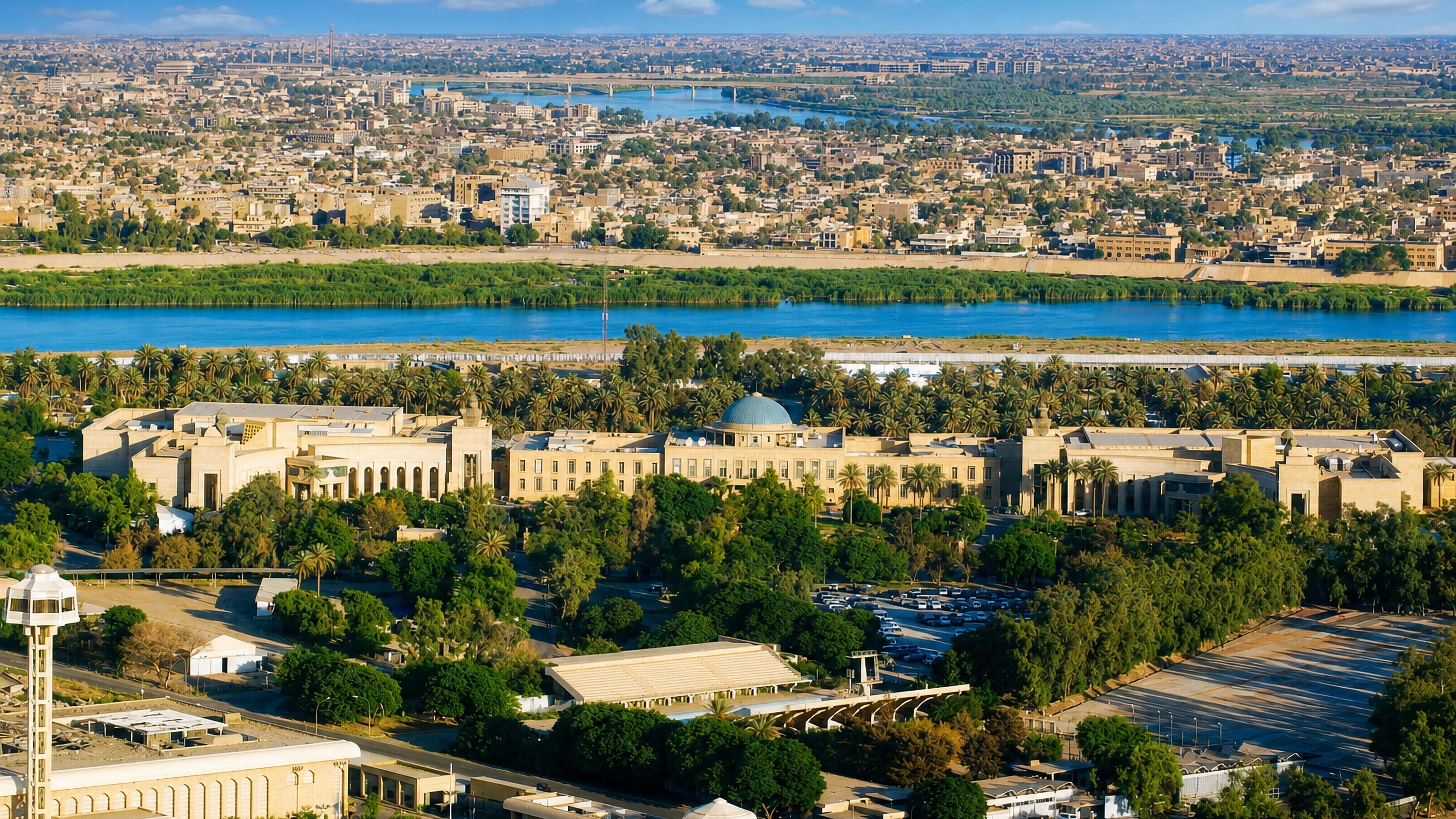 Aerial view of Baghdad with the Tigris River curving past green banks and a sprawling low-rise city under clear skies