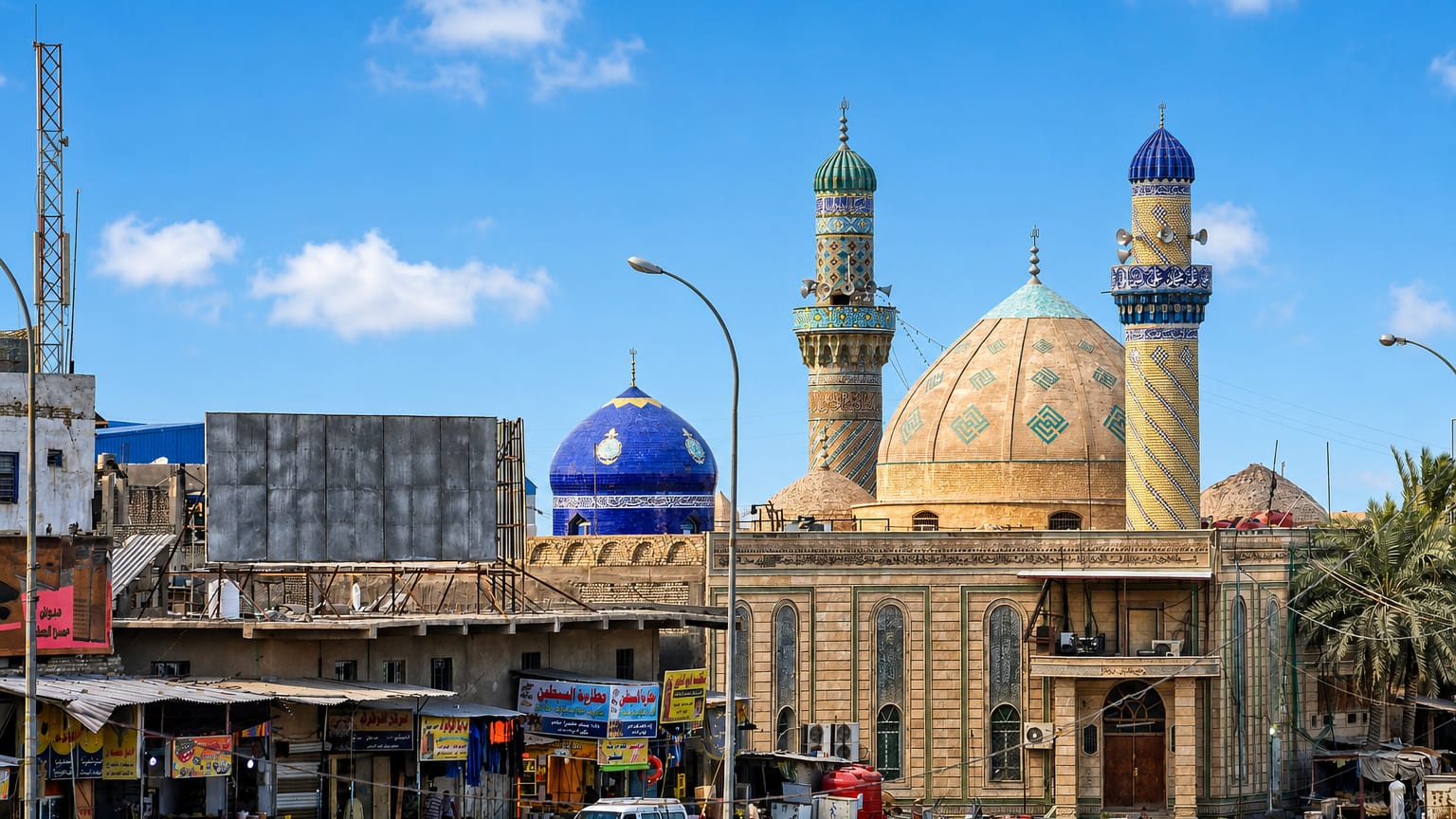 Ornate mosque with tiled domes and twin minarets above a busy market street in Basra, Iraq.