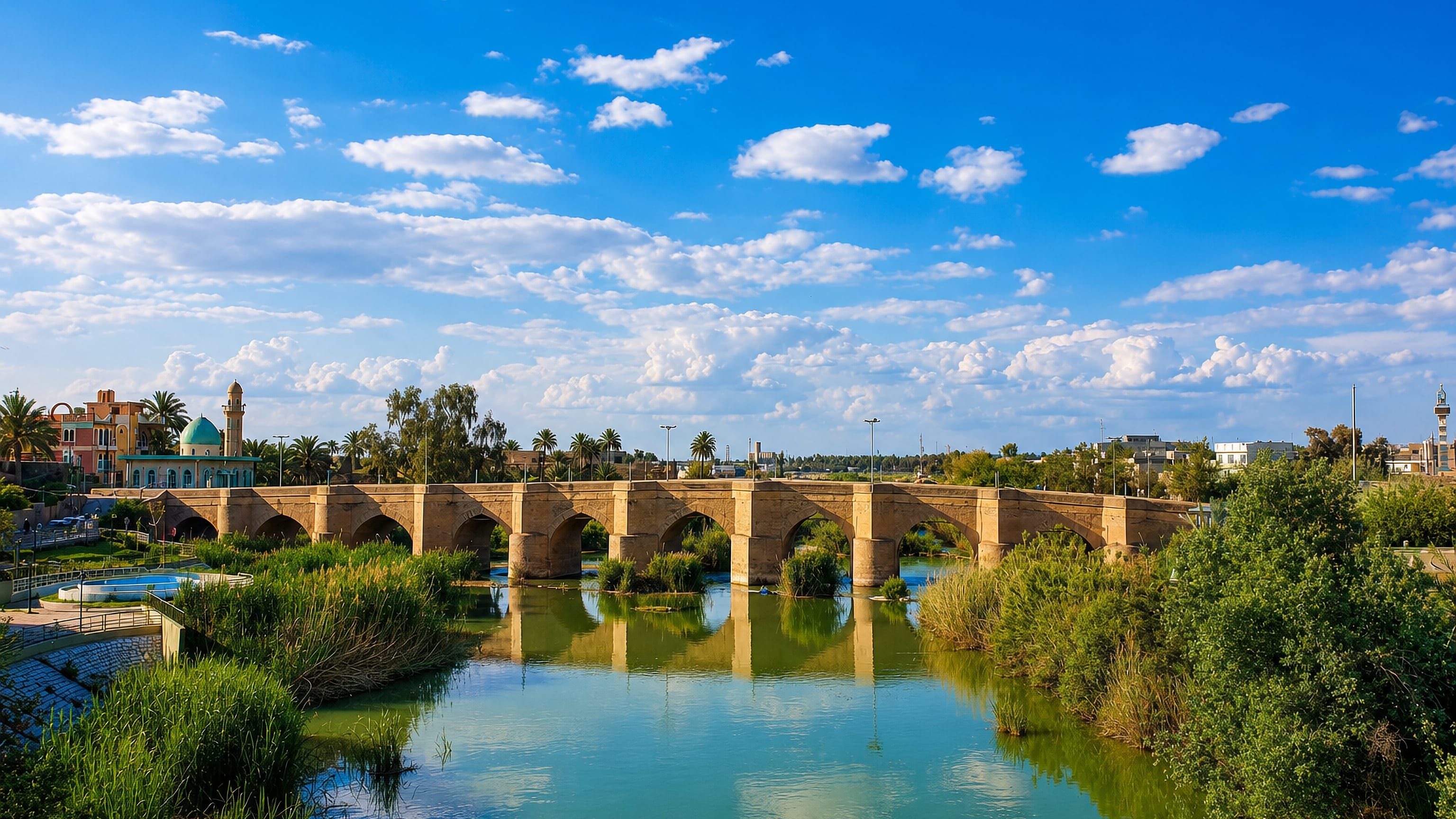 The historic stone arch bridge over the Alwand River in Khānaqīn, Iraq, with a domed mosque beyond.
