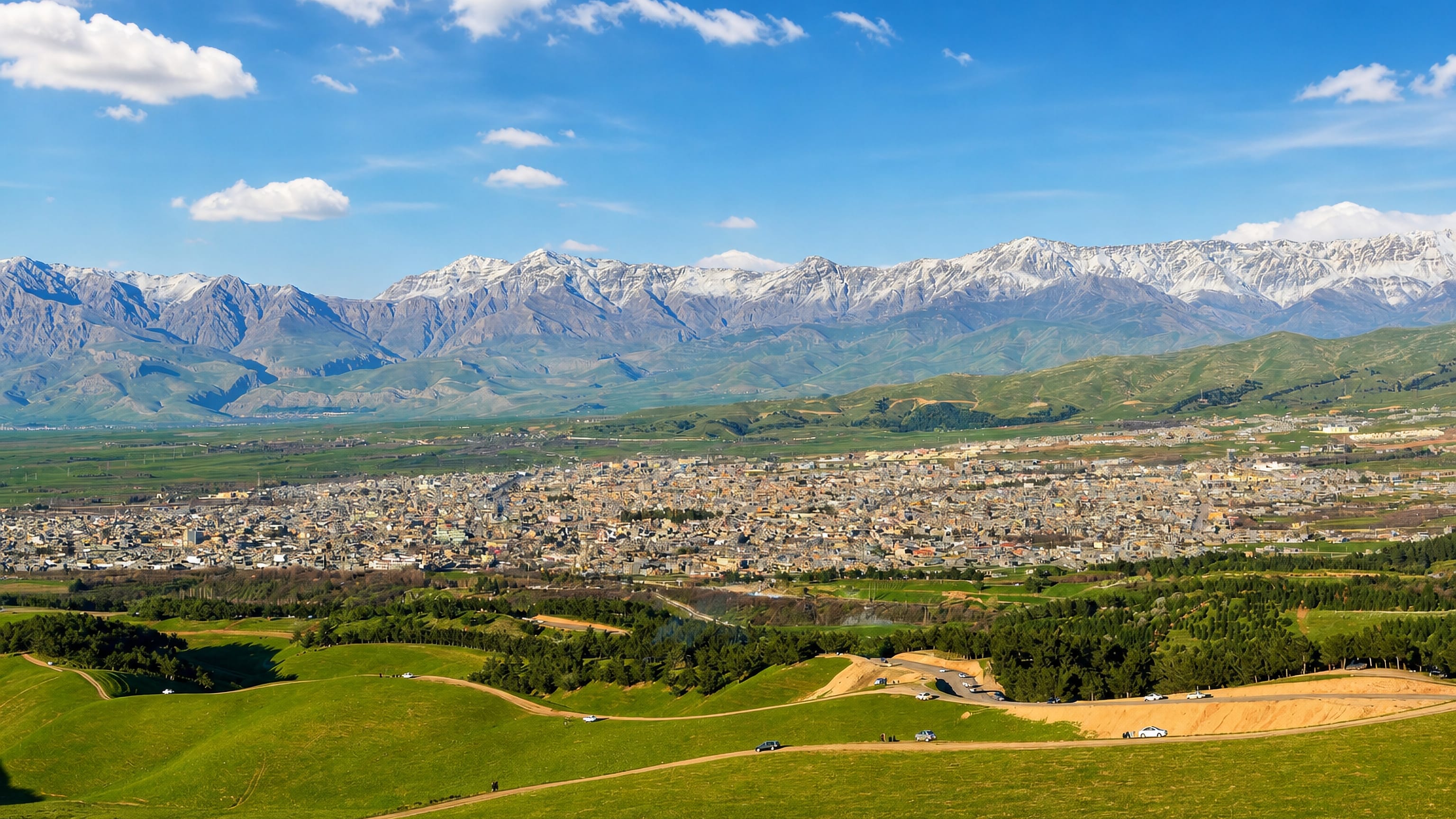 Halabja, Iraq, spread across a green plain below the snow-capped Zagros mountains.