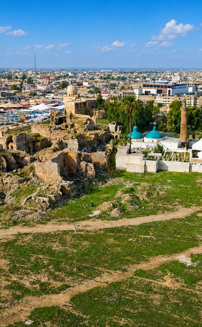 Kirkuk Citadel mound with ruined walls and a green-domed shrine and minaret above the surrounding city.