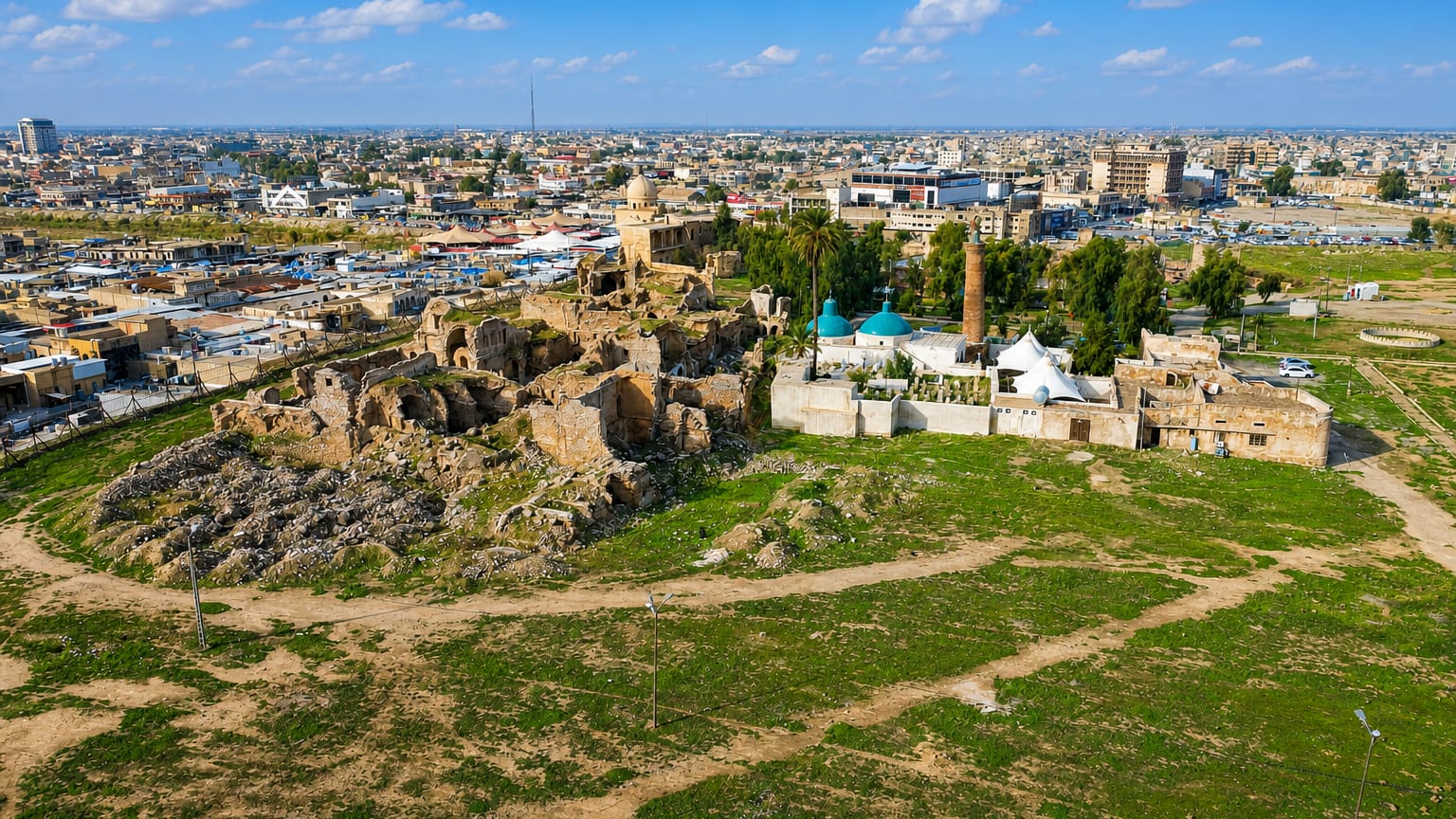 Kirkuk Citadel mound with ruined walls and a green-domed shrine and minaret above the surrounding city.