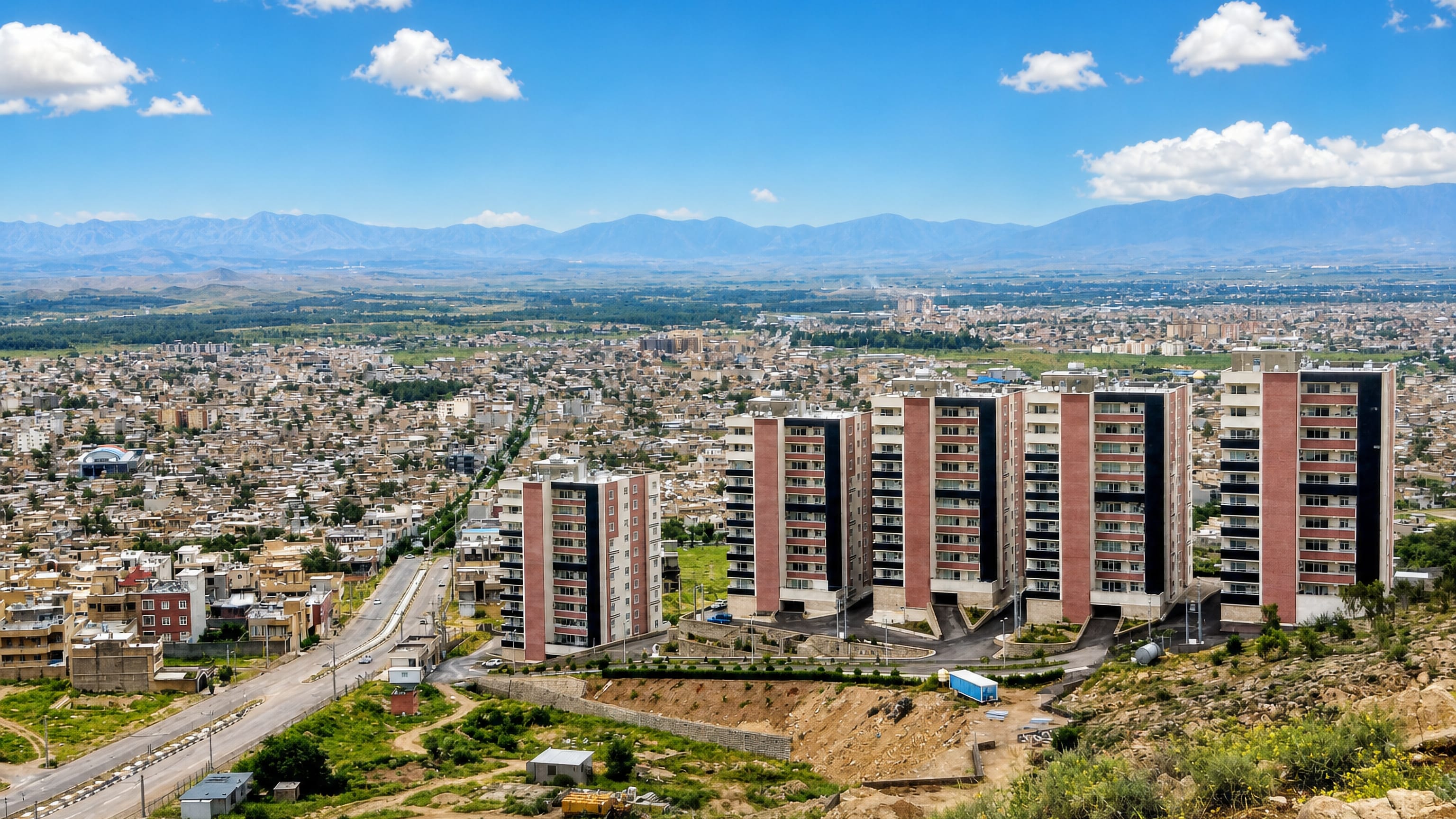 Hillside view over Jahrom, Iran, with new apartment towers, low-rise streets and mountains beyond.