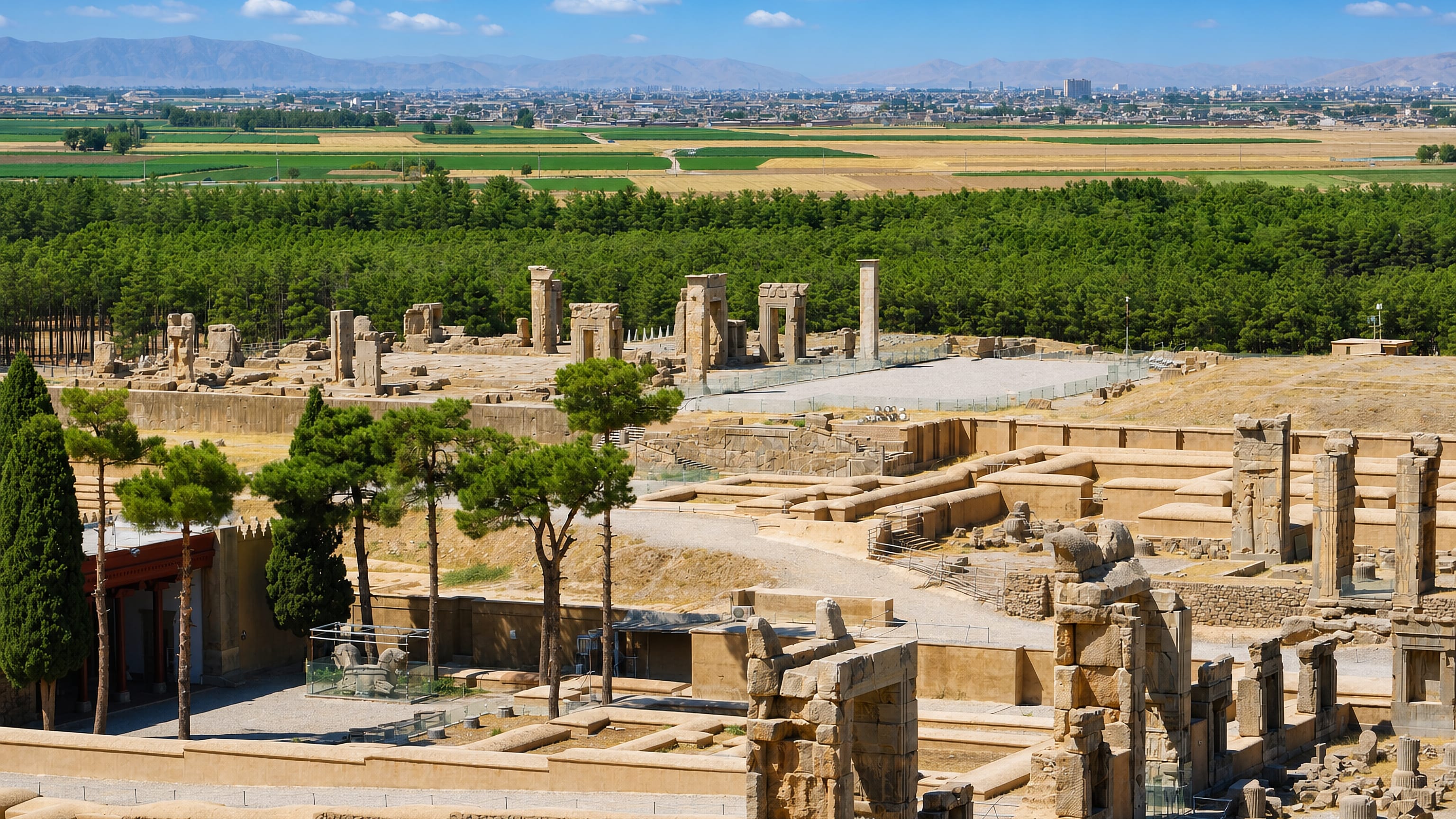 The Persepolis ruins above the Marvdasht plain, with the Iranian city and Zagros foothills beyond.