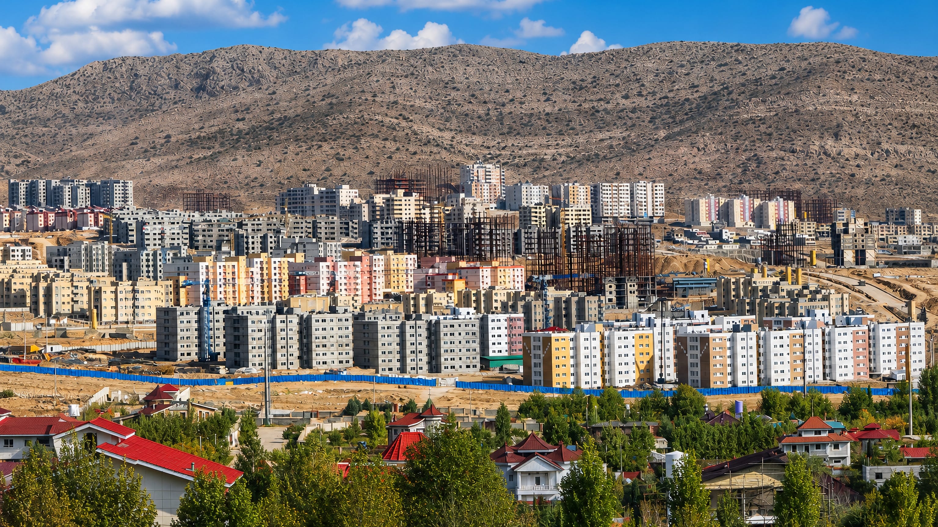 Rows of new apartment blocks in Shahr-e Sadra, Iran, below a bare mountain ridge, with villas in front.