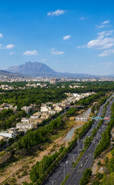 Aerial view of Shiraz, Iran, set in a green valley with a highway and river beneath distant mountains