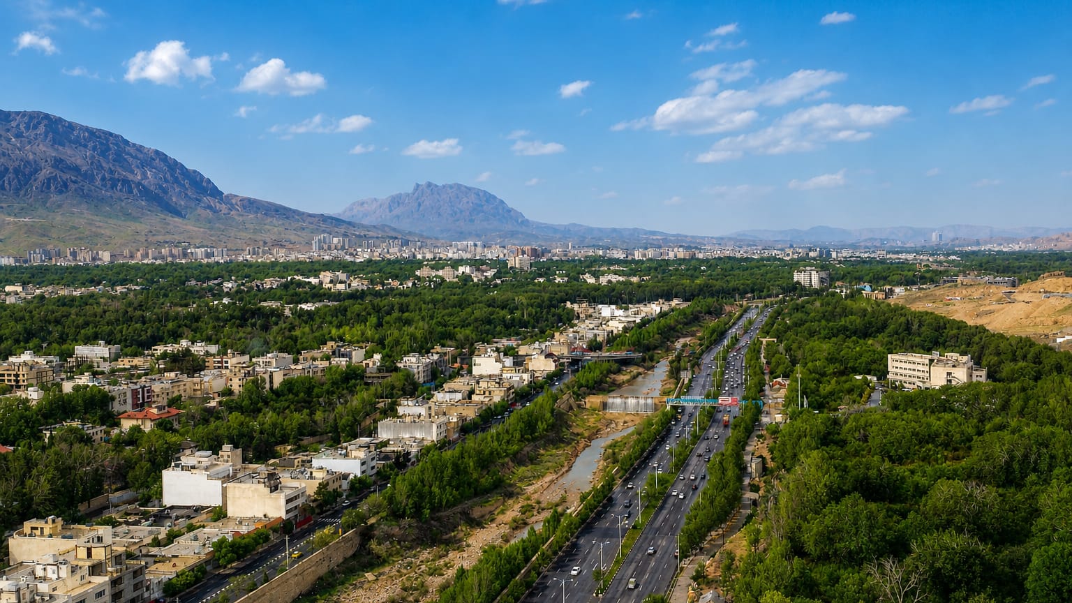 Aerial view of Shiraz, Iran, set in a green valley with a highway and river beneath distant mountains