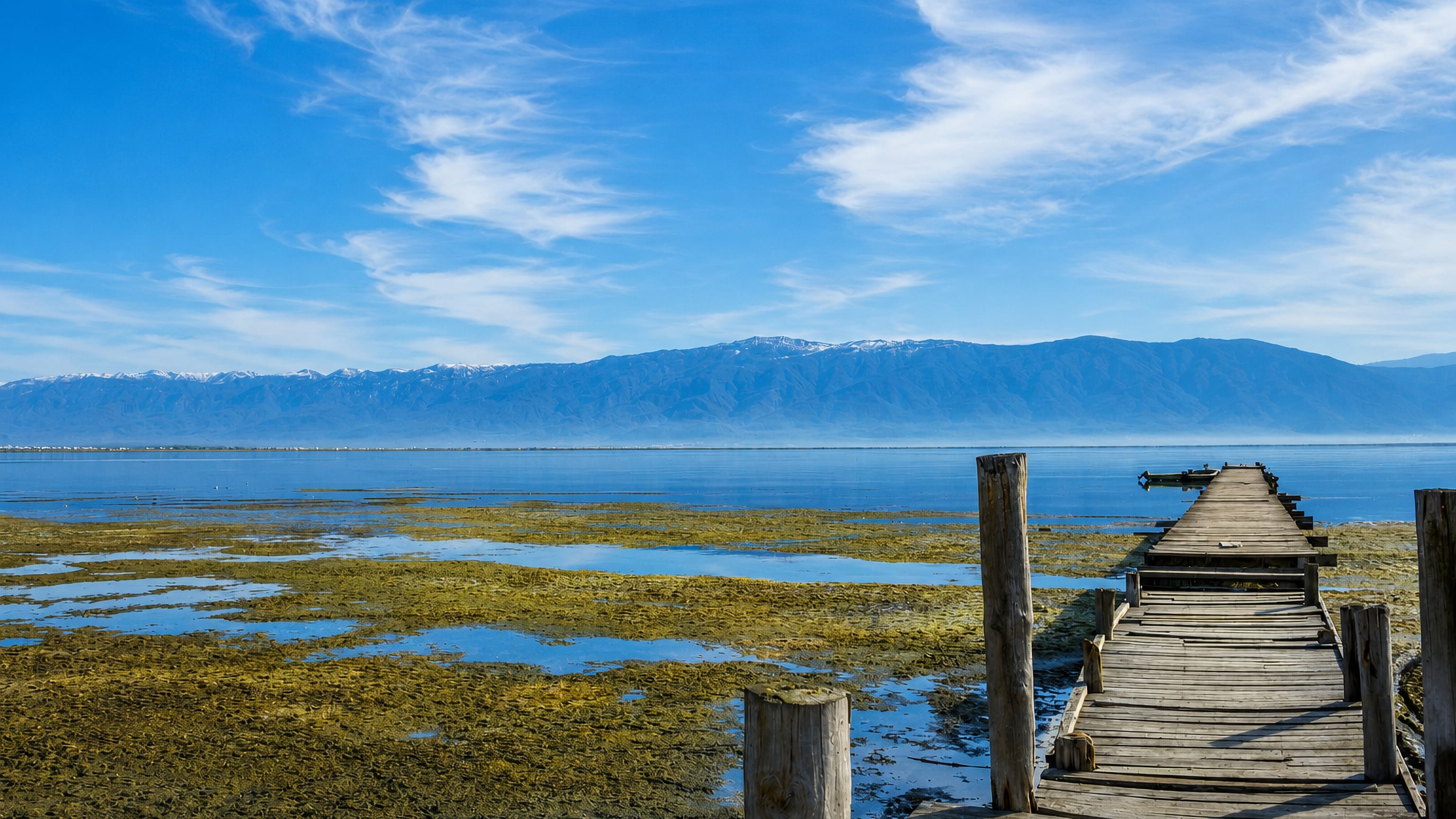 Wooden jetty reaching into the shallow Caspian bay at Bandar-e Torkaman, Iran, with mountains beyond.