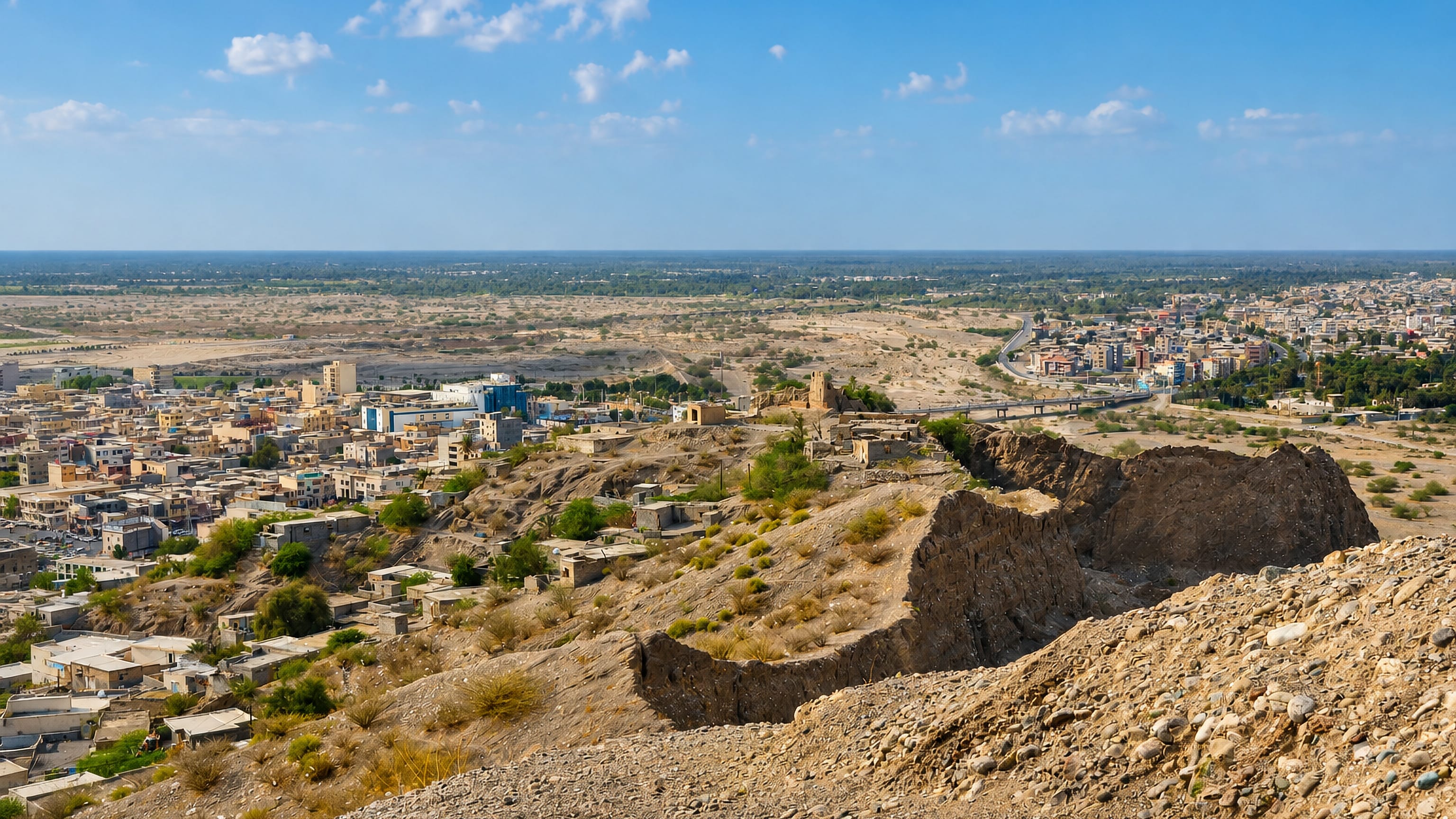 Ruined mud-brick citadel walls on a ridge above Minab, Iran, with the town spreading across the plain