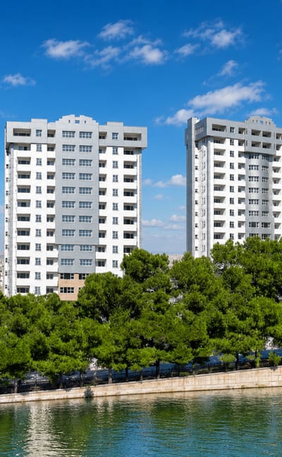 Modern white residential towers above pine trees along a riverbank in Isfahan, Iran.