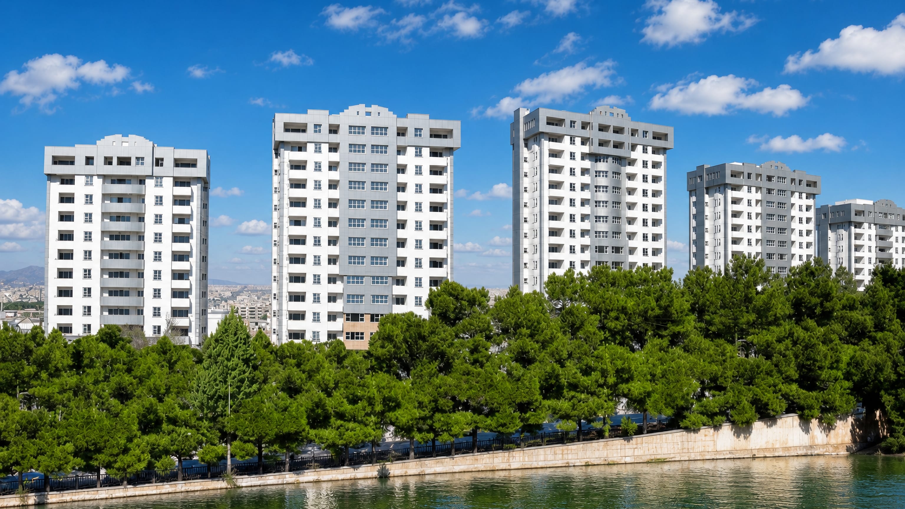 Modern white residential towers above pine trees along a riverbank in Isfahan, Iran.