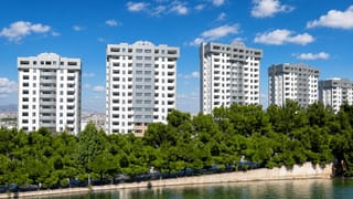 Modern white residential towers above pine trees along a riverbank in Isfahan, Iran.