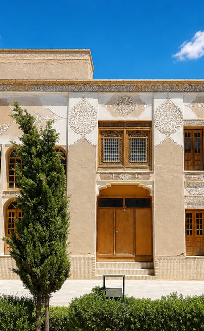 Traditional Persian courtyard house with carved stucco panels and wooden windows in Shahr-e Bābak, Iran.