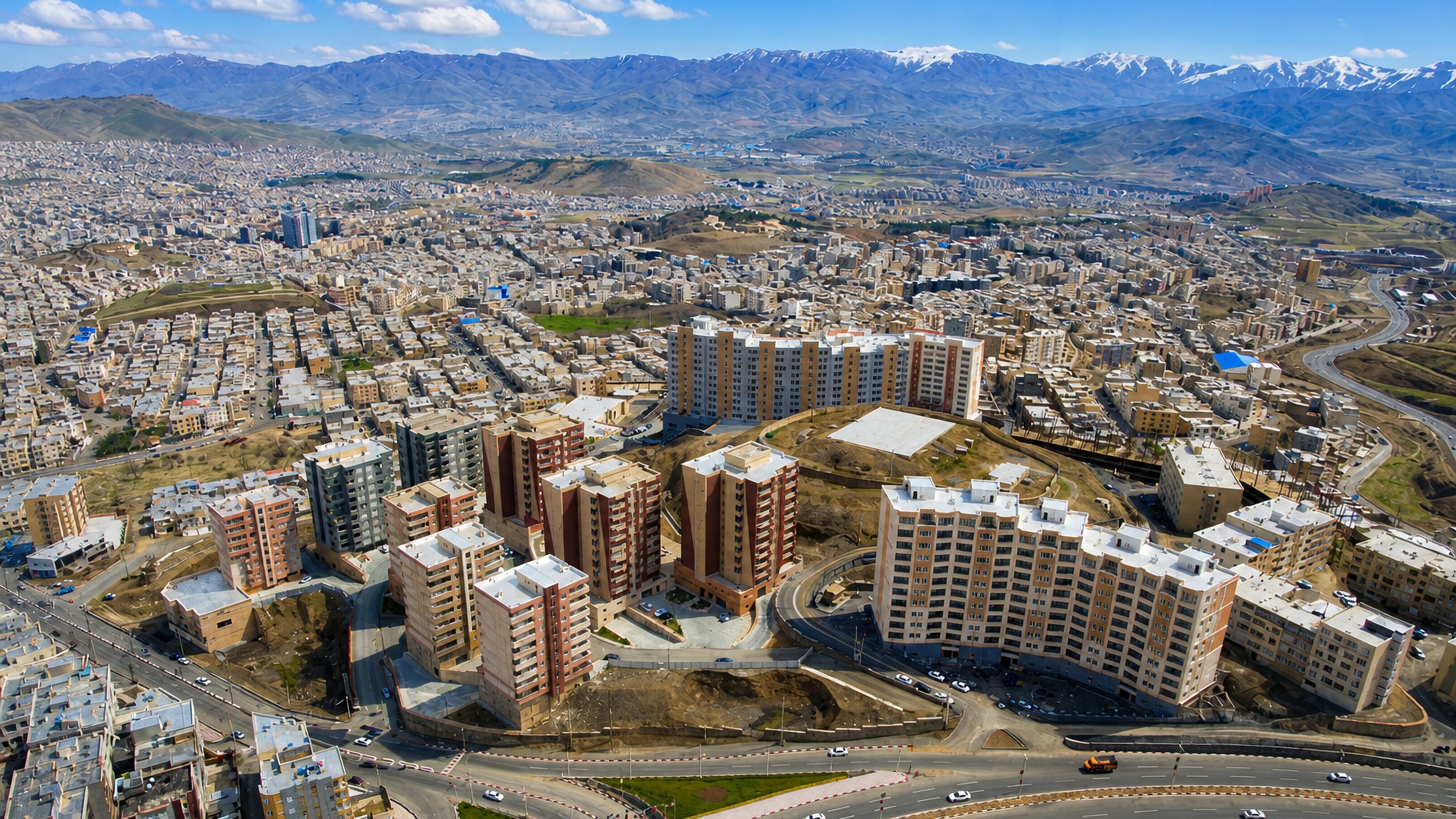 Aerial view of Sanandaj's apartment blocks and highways with the snow-capped Zagros ranges rising behind.