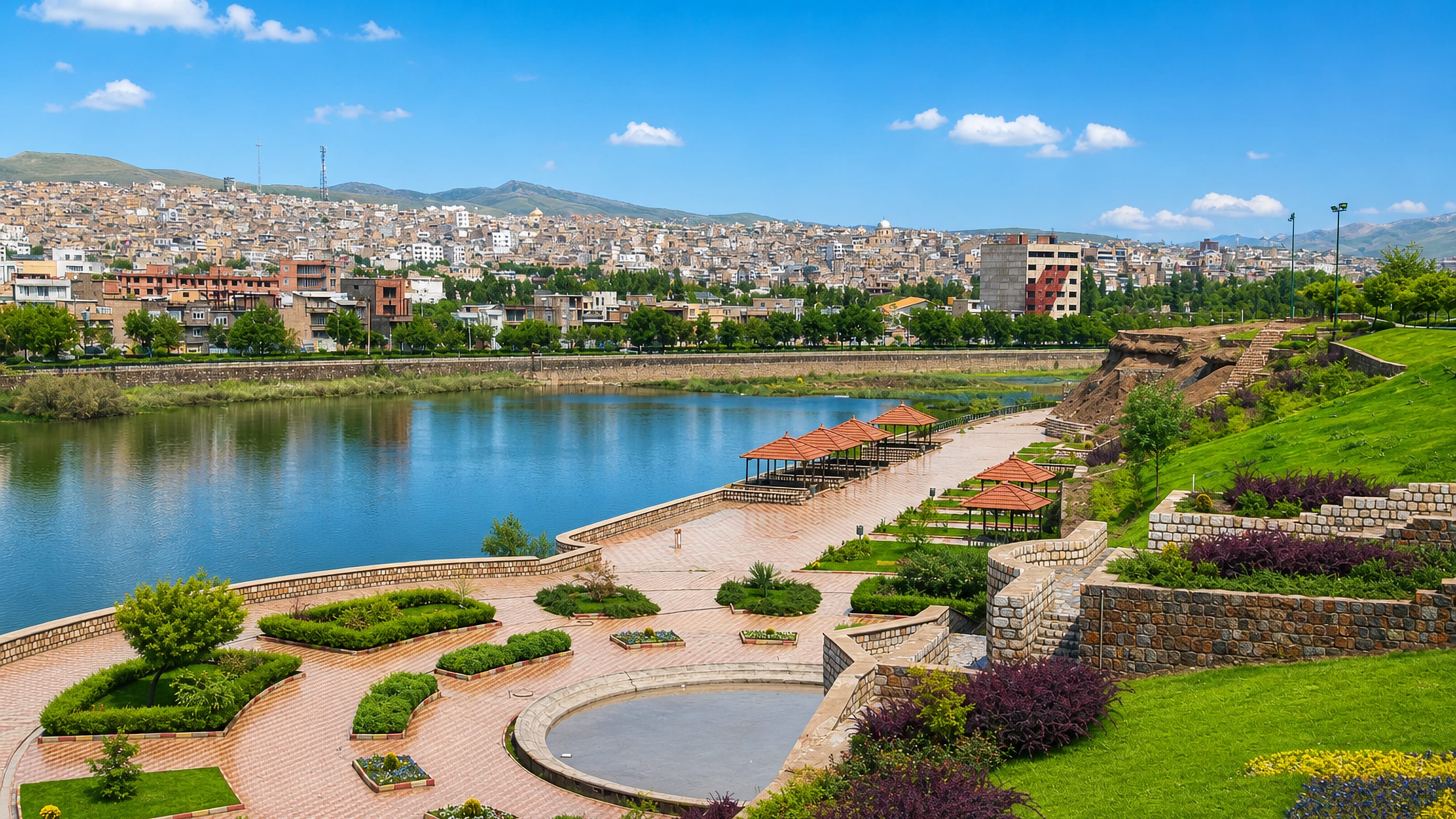 Saqqez, Iran, a landscaped riverside park with pergolas below hillside housing and distant mountains.