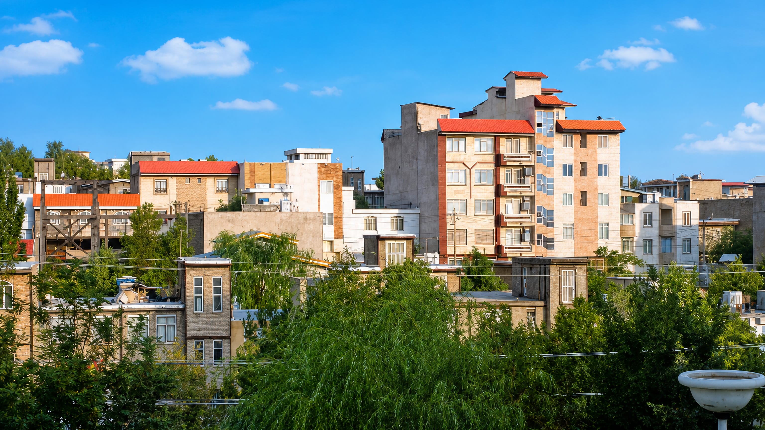 Apartment blocks with red-tiled roofs rise above leafy streets in Borujerd, Lorestan, Iran.