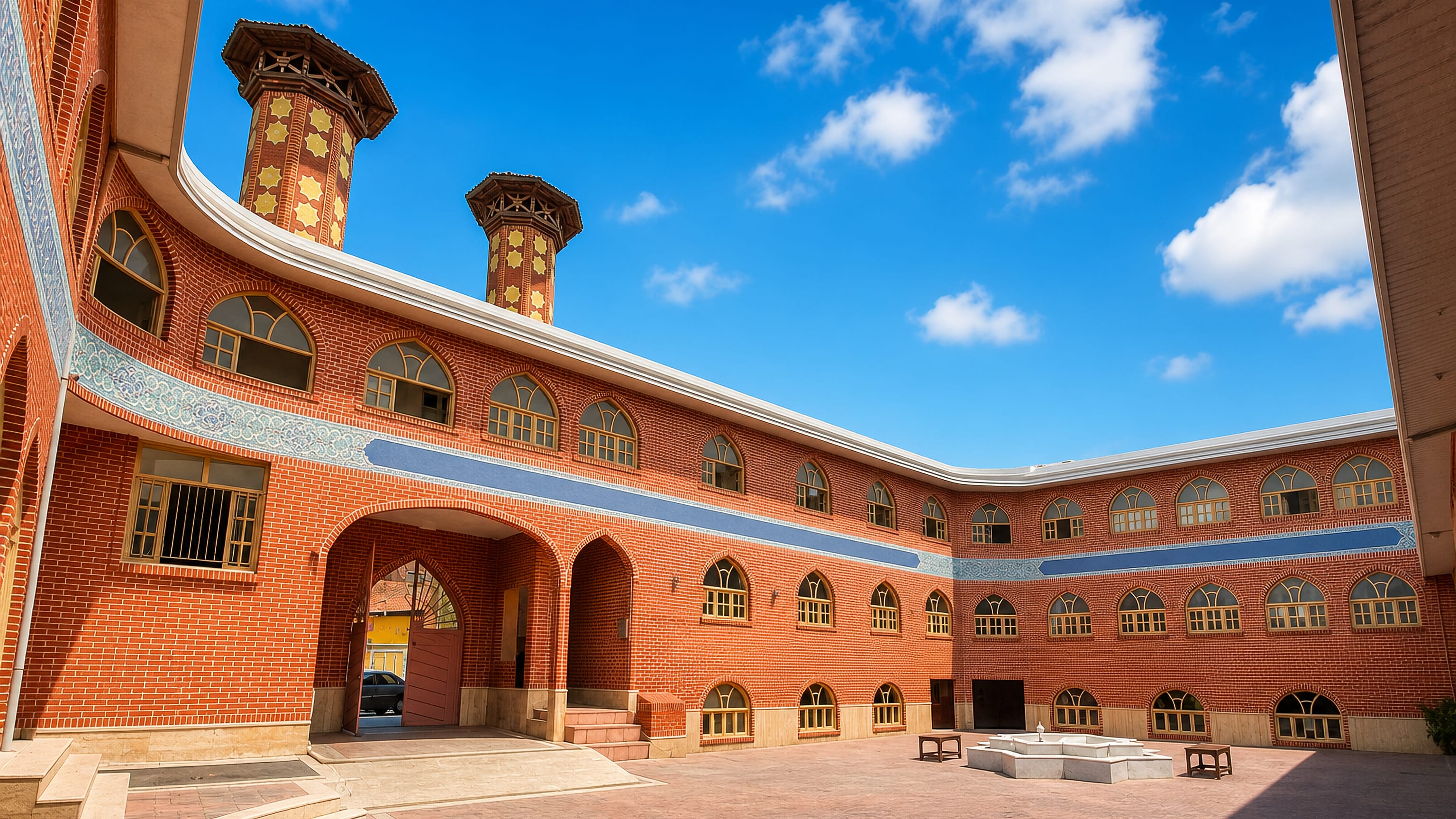 Brick courtyard and twin minarets of a historic mosque in Babol, northern Iran, under a bright blue sky.