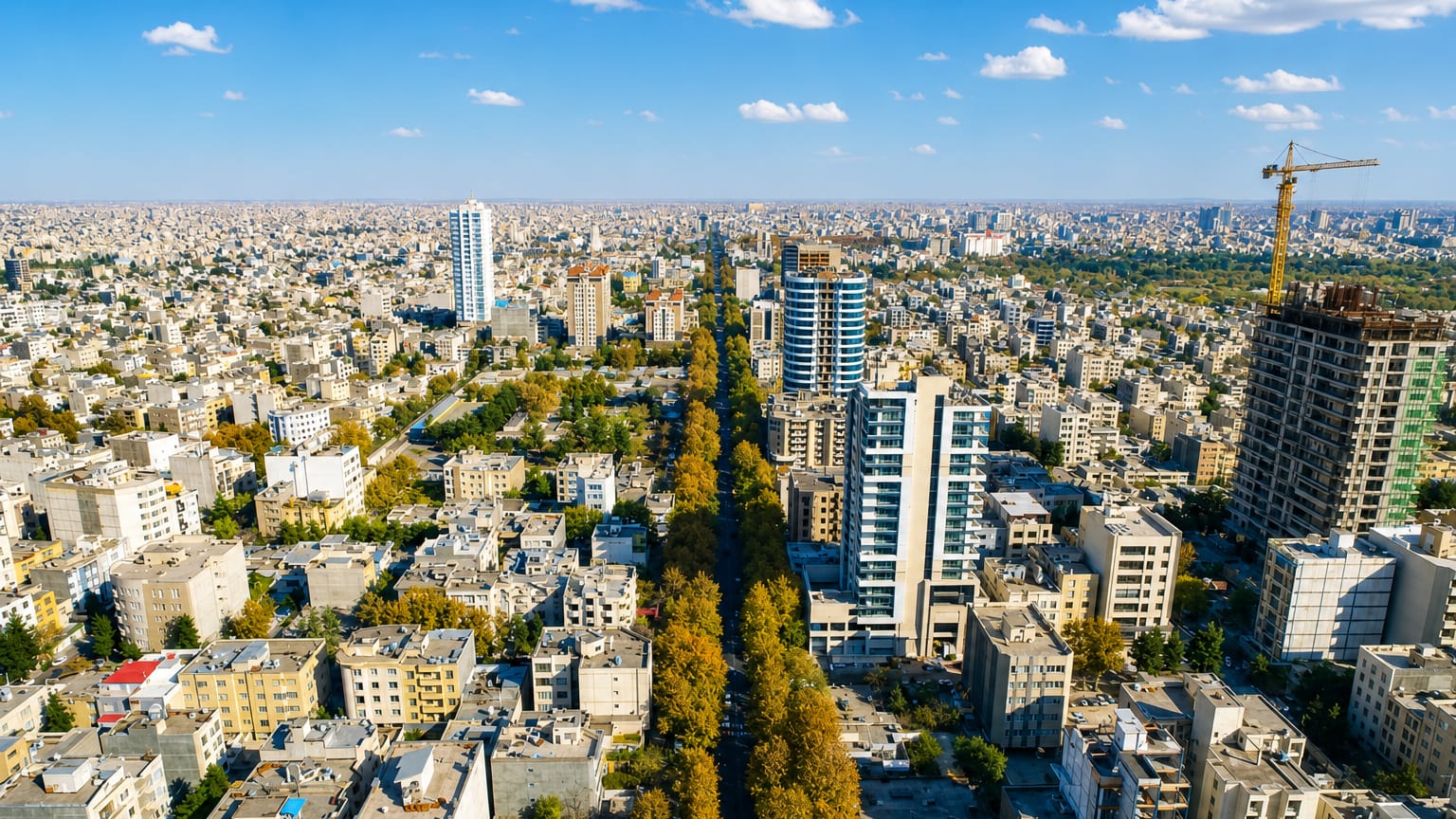 Aerial of Mashhad's sprawling mid-rise city and a tree-lined boulevard under a clear sky.