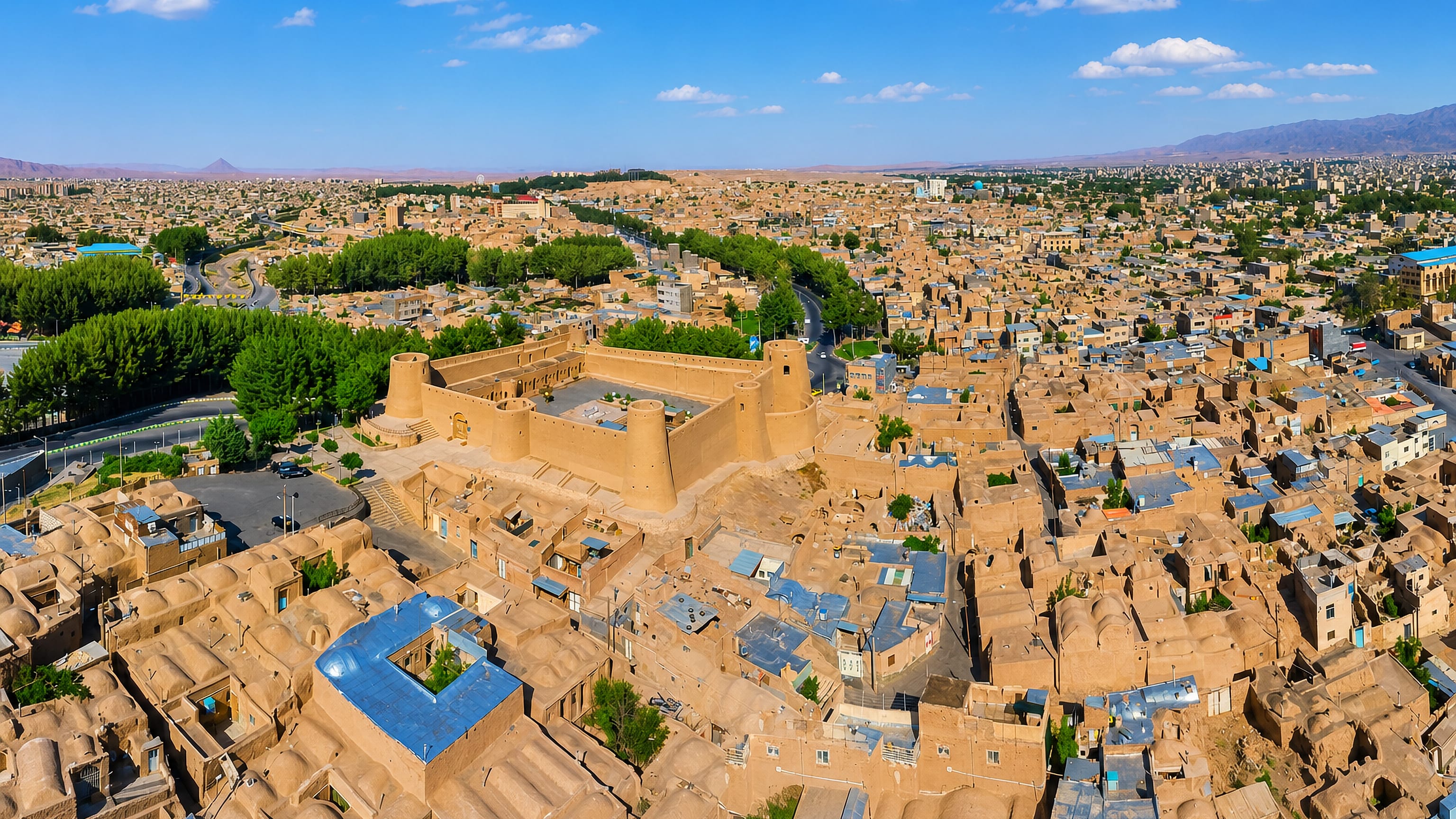 Aerial view of Bīrjand, Iran, with a mud-brick citadel amid flat-roofed adobe houses and desert hills.