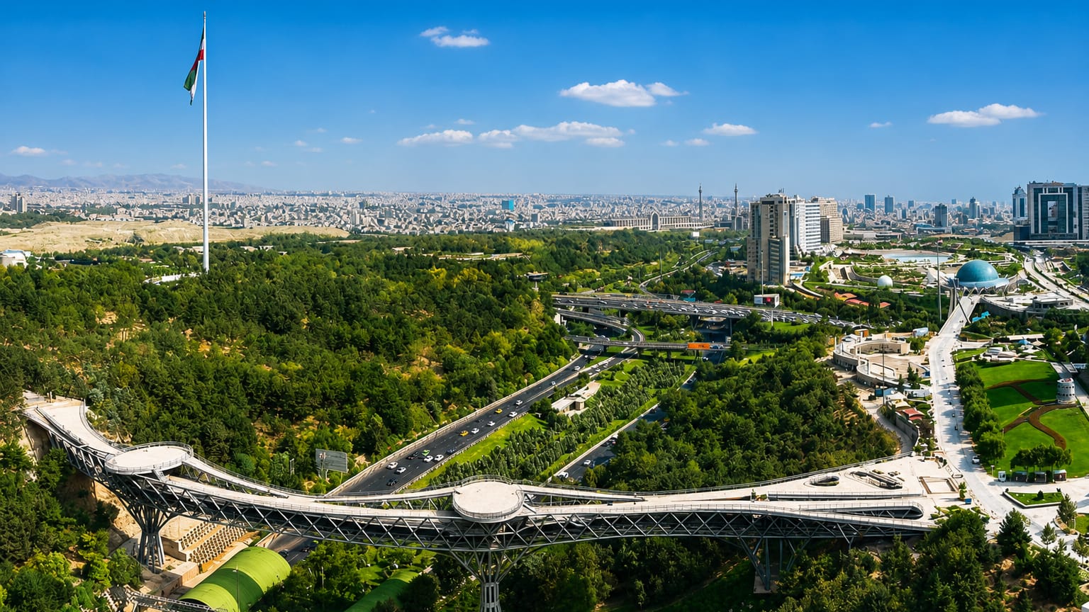 Tehran's Tabiat Bridge and green parkland in Abbas Abad, with the Iranian flag and city skyline beyond.