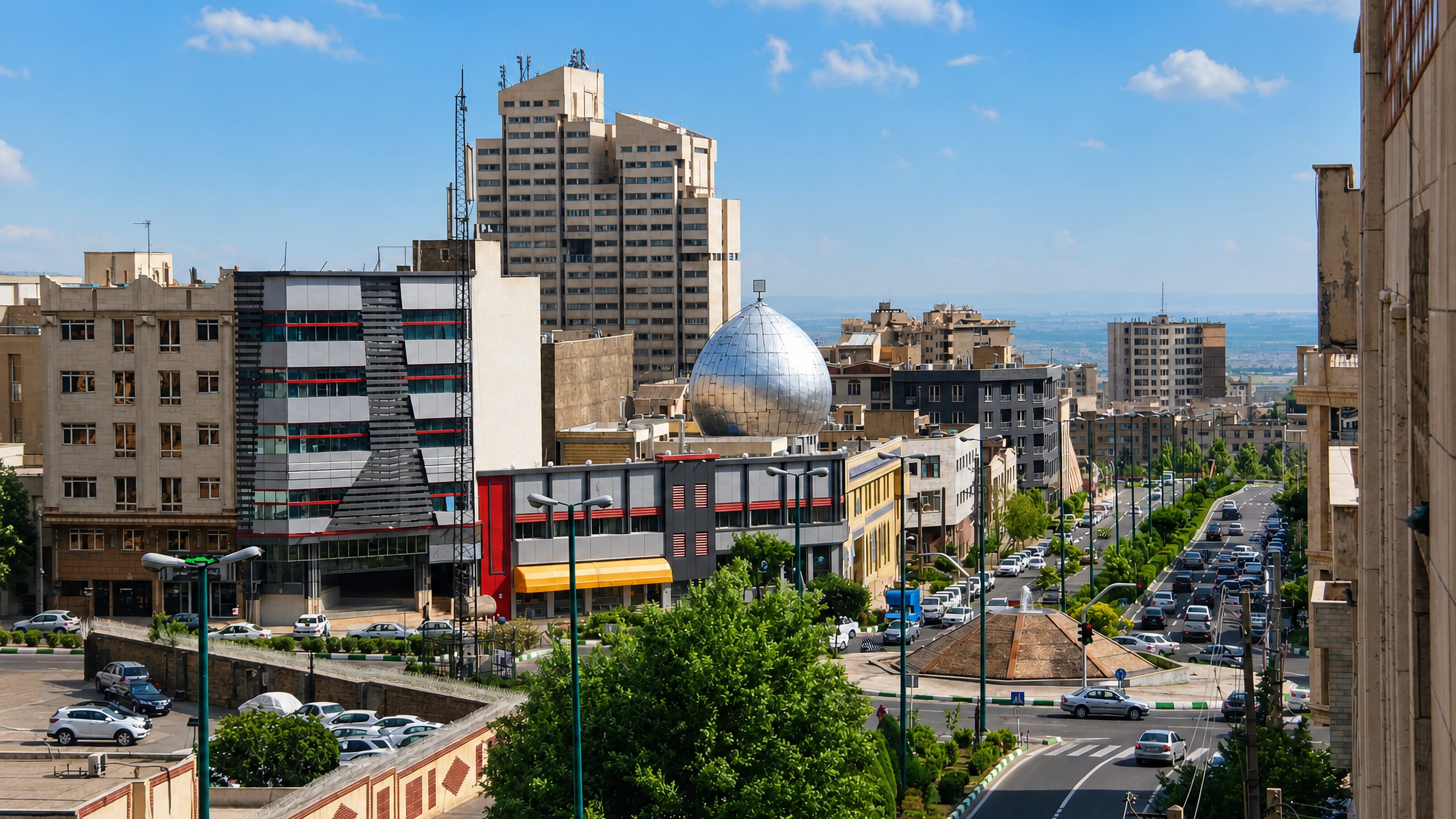 Tree-lined avenue in Punak, northwest Tehran, with mid-rise towers, a mirrored dome and the Alborz foothills beyond.