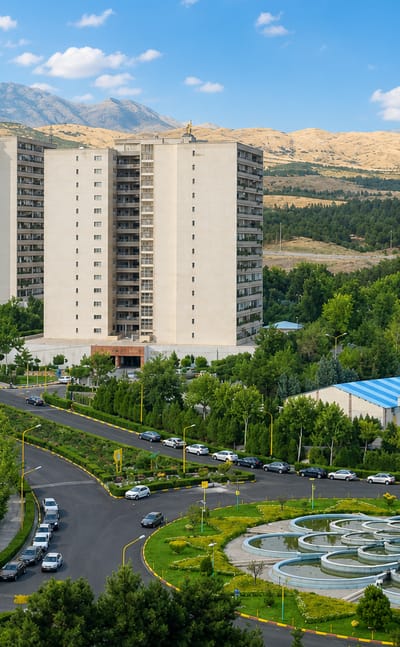 Beige residential tower blocks below the arid Alborz mountains with a landscaped fountain in Tehranpars, Tehran