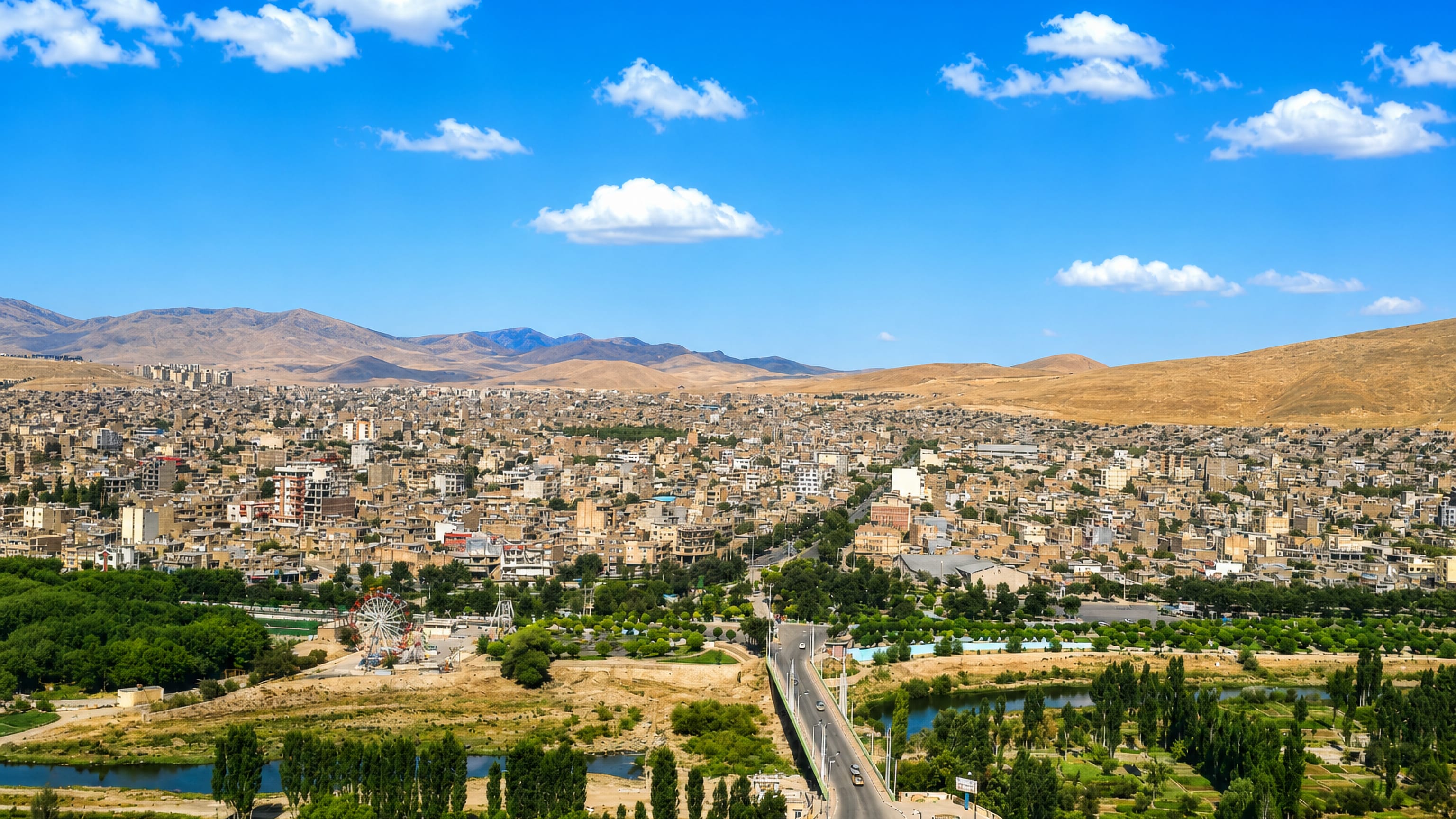 Bukan, Iran, spread across arid hills above a tree-lined river, bridge and farm plots at the town's edge.
